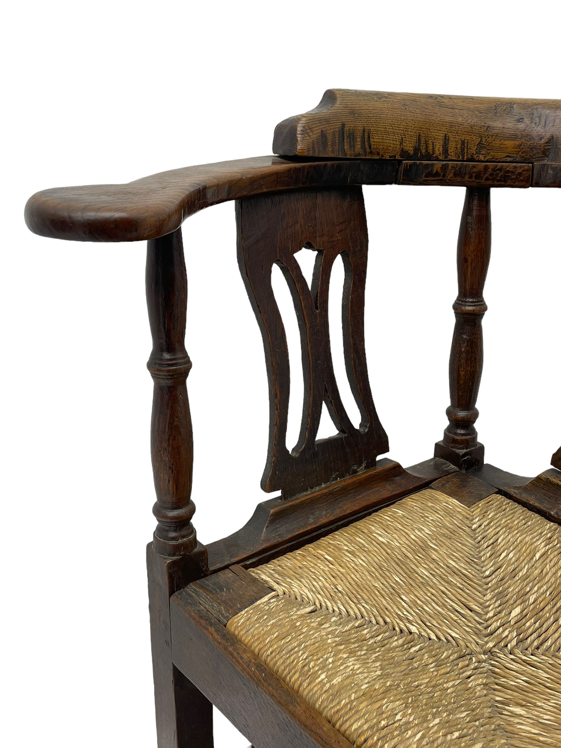 18th century country elm and oak corner chair, the shaped cresting rail terminating to swept arm resets, supported by turned columns and pierced shaped splats, over a drop-in rush seat, raised on square supports united by box stretcher