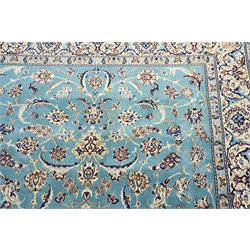 Central Persian Nain hand-knotted carpet, soft sky blue ground with central cusped medallion of radiating palmette form, issuing scrolling vine work, arabesques, and delicate floral sprays, spandrels of conforming design, main border of ivory ground decorated with scrolling vine work palmettes and stylized floral motifs, flanked by narrow guard stripes, with cotton fringe ends 