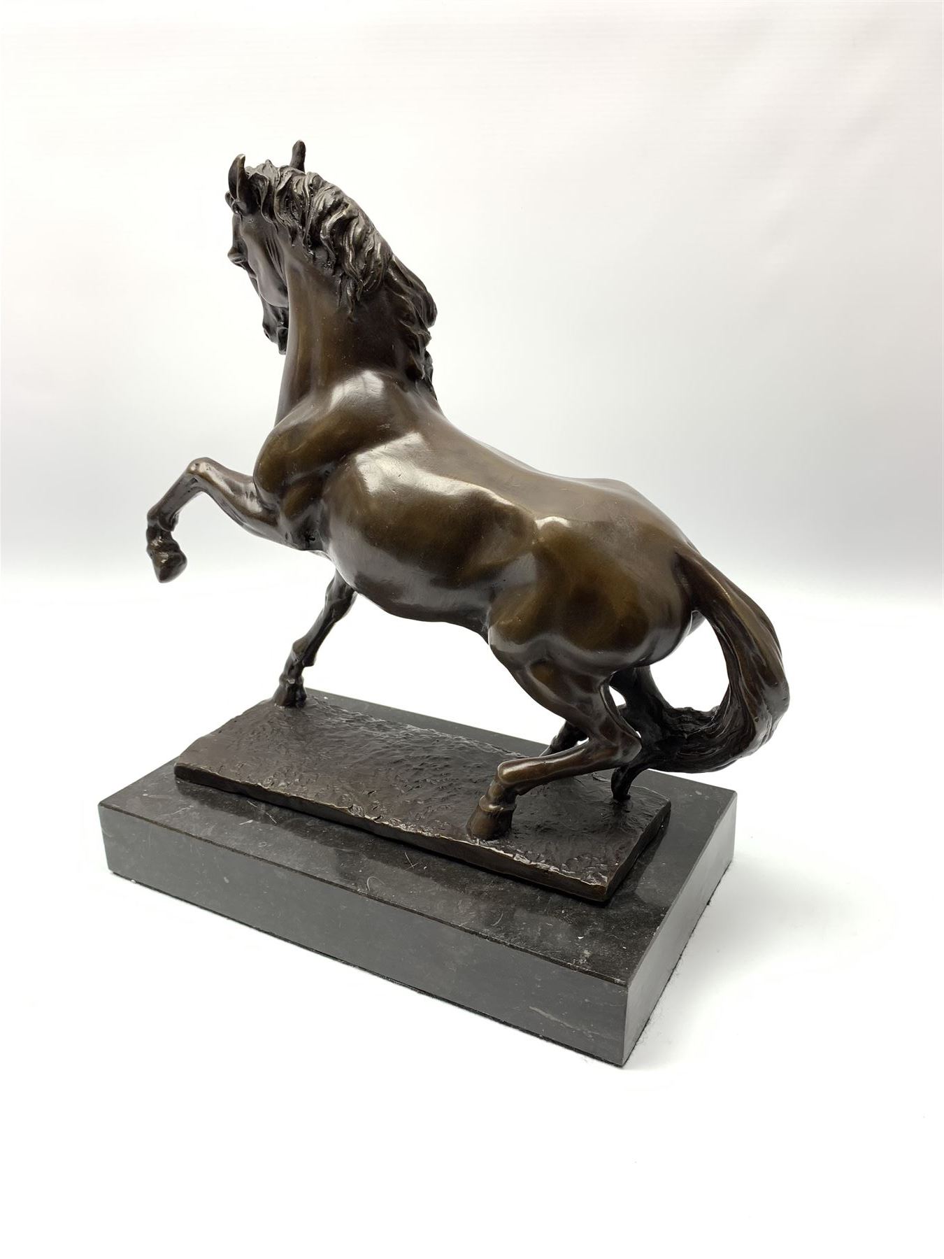 Bronze figure modelled as a prancing horse, upon a naturalistically modelled rectangular base, and black marble plinth, H34.5cm, L31cm