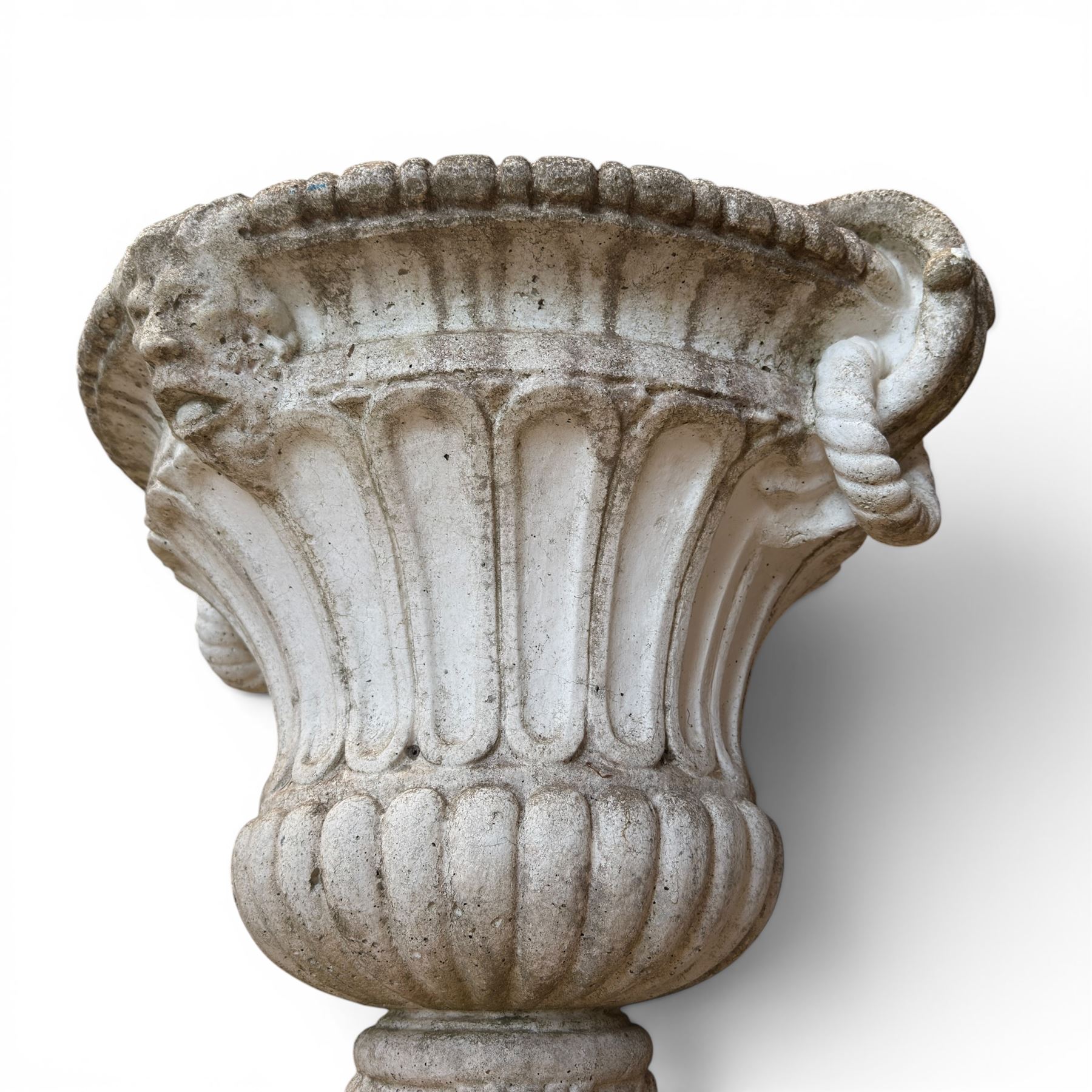 Pair of Neoclassical design cast stone garden urns, each of campana form with fluted body and gadrooned underbelly, decorated with faun/satyr opposing masks and ropetwist handles, with floral and mask design to the socles, raised on square bases, finished in weathered white patina