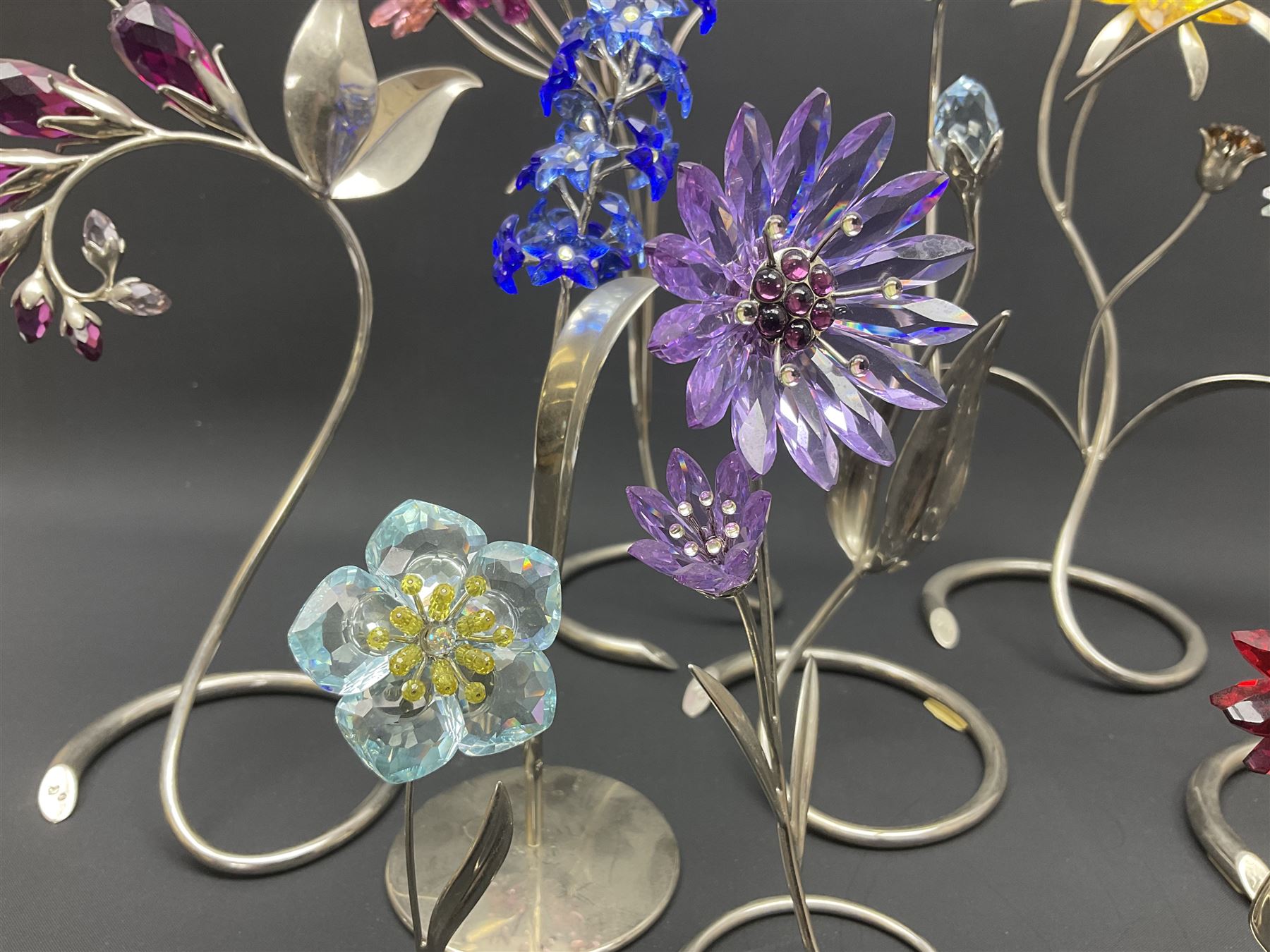 Eleven Swarovski Crystal flowers, to include violet, sunflower, delphinium, forget-me-not and lily-of-the-valley, each on stylised metal stems, tallest H23cm