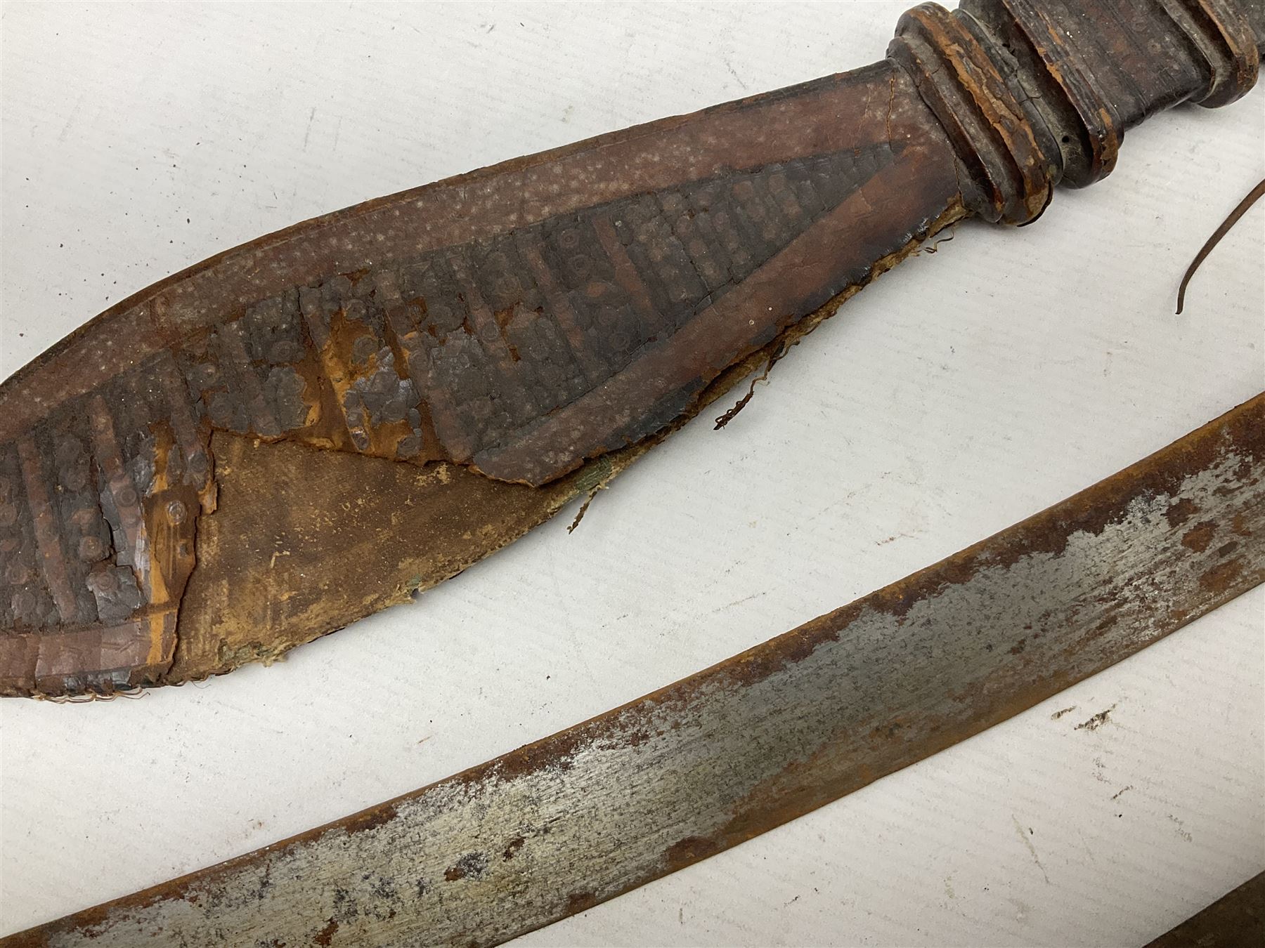 Mandingo sword, the 63cm plain curving steel blade marked with a horses head and the initials G.S.; leather covered grip with metal ribbed spherical pommel; in decorative leather leaf scabbard mounted with tassels and roundels L84cm overall; and a North African flyssa sword in poor condition with wooden scabbard (2)