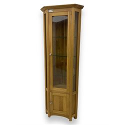 Contemporary light oak corner display cabinet, projecting cornice over single glazed door enclosing three glass shelves, the base fitted with panelled cupboard enclosing single oak shelf, on stile supports