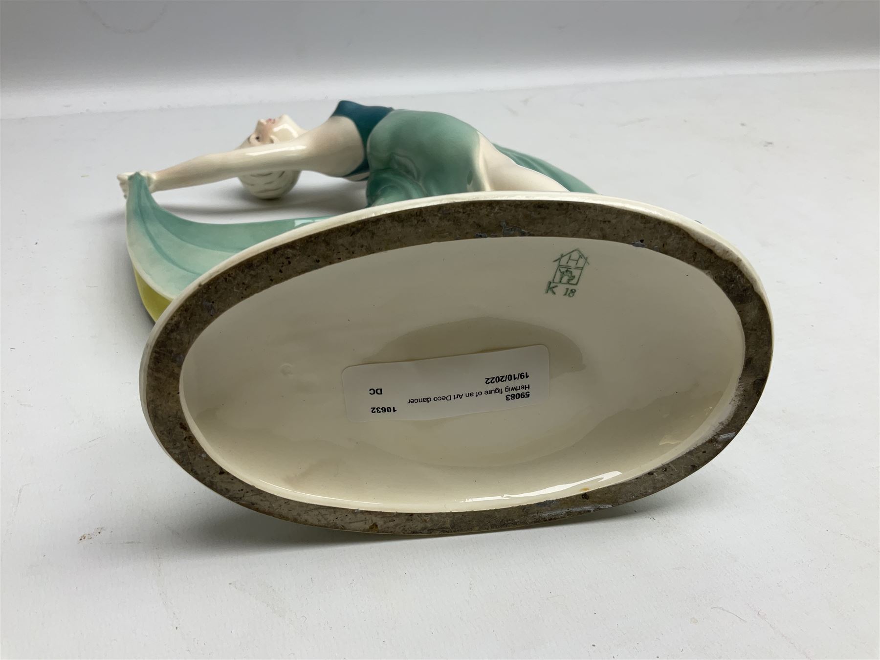 Early 20th century Hertwig Katzhütte figure of an Art Deco lady dancing, wearing a green, blue and yellow dress, stood upon on a domed plinth, with green cat H house printed mark beneath, H32cm