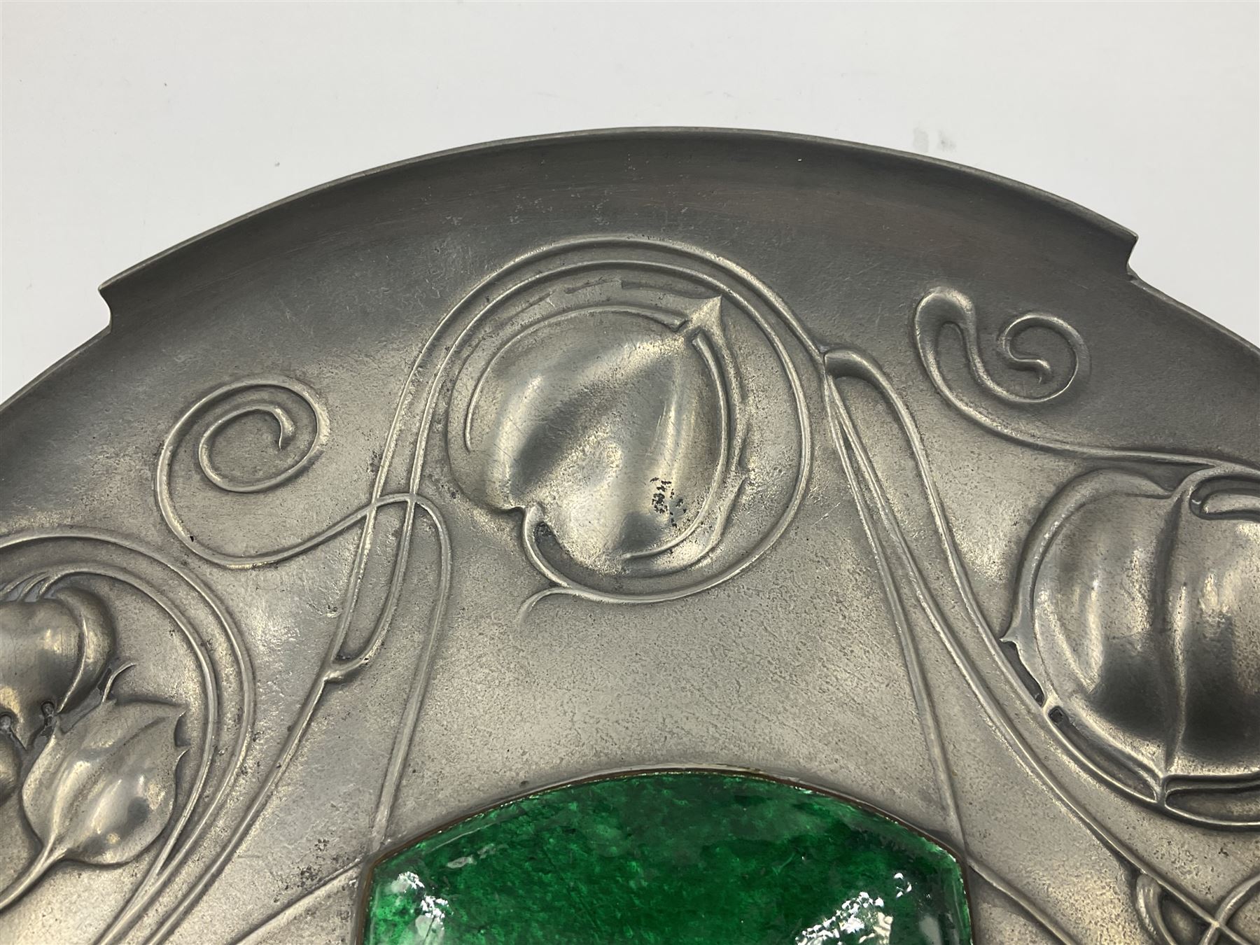 Liberty & Co Tudric pewter Bollelin tray, designed by Archibald Knox, of circular form with shaped edge, cast in relief with foliate tendrils surrounding a green enamel cartouche, impressed beneath Made by Library & Co English Pewter 044, D25.5cm