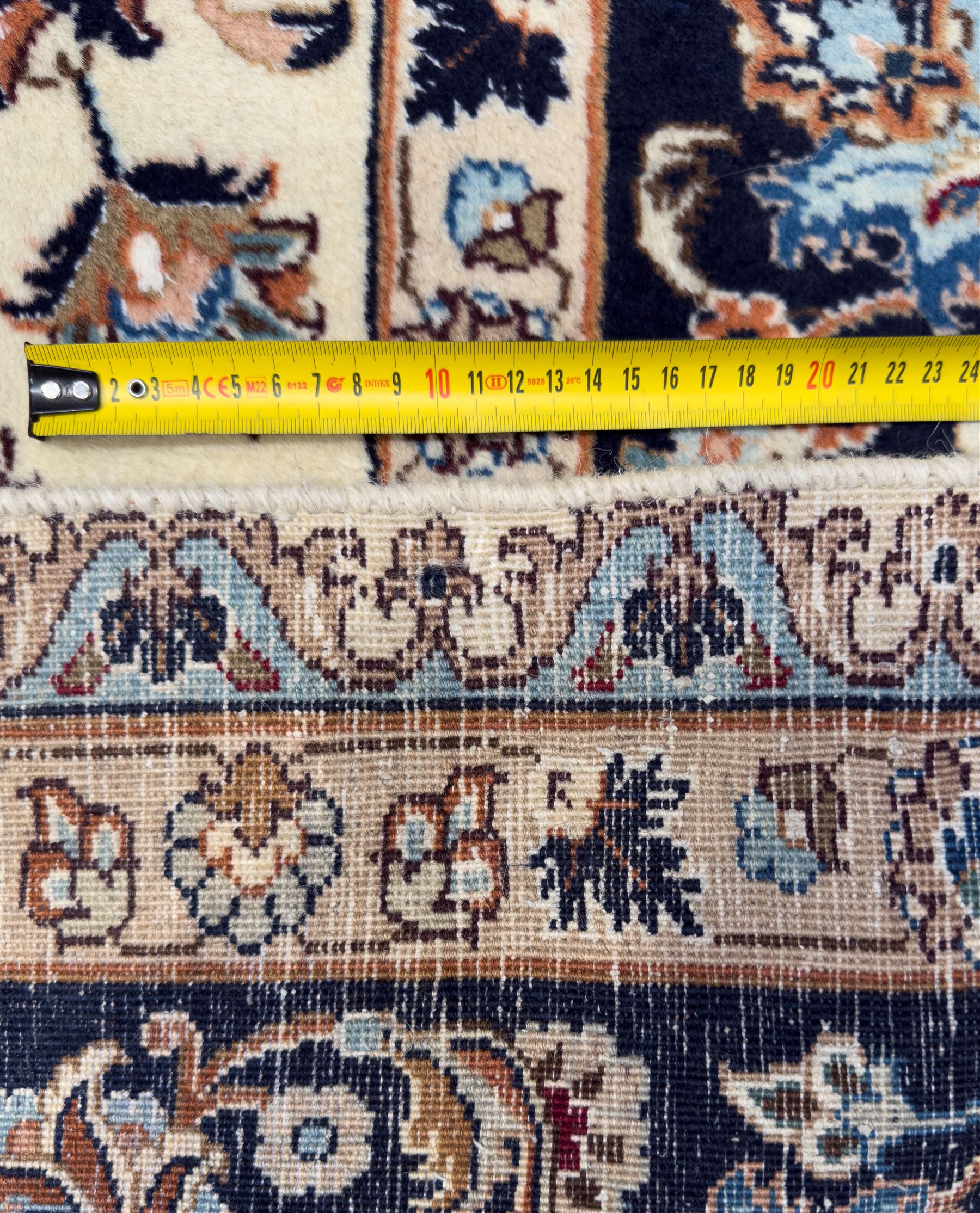 North East Persian Meshed hand-knotted rug, ivory field with scrolling vines, palmettes, and rosettes in shades of blue and brown, within a dark blue border of palmettes and flowerheads between multiple guard stripes, with cotton fringe ends  