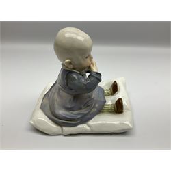 Early 20th century Meissen figure, circa 1905-1924, designed by Konrad Hentschel, modelled as a baby seated upon a cushion wearing a merging purple and blue dress, green and white striped leggings and brown shoes, with blue crossed swords mark and incised model number U 150 beneath, H12.5cm

