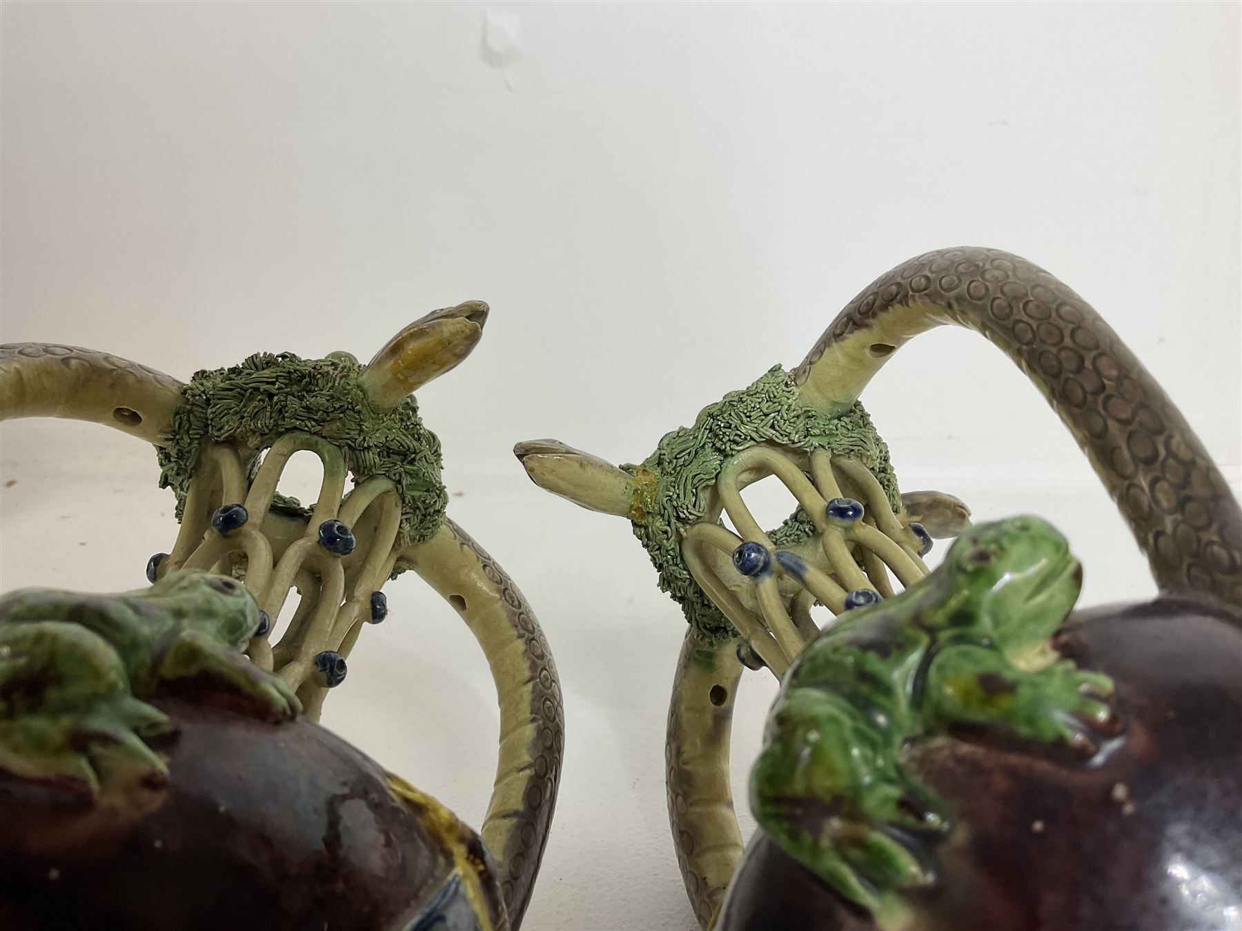 Pair of 19th century Portuguese Palissy style Majolica puzzle jugs, attributed to Manuel Mafra, with mossy rim and pierced lattice neck, twin handles in the form of snakes and the body decorated with frogs, lizards, and moths on a mottled brown glazed ground, unmarked, H20cm