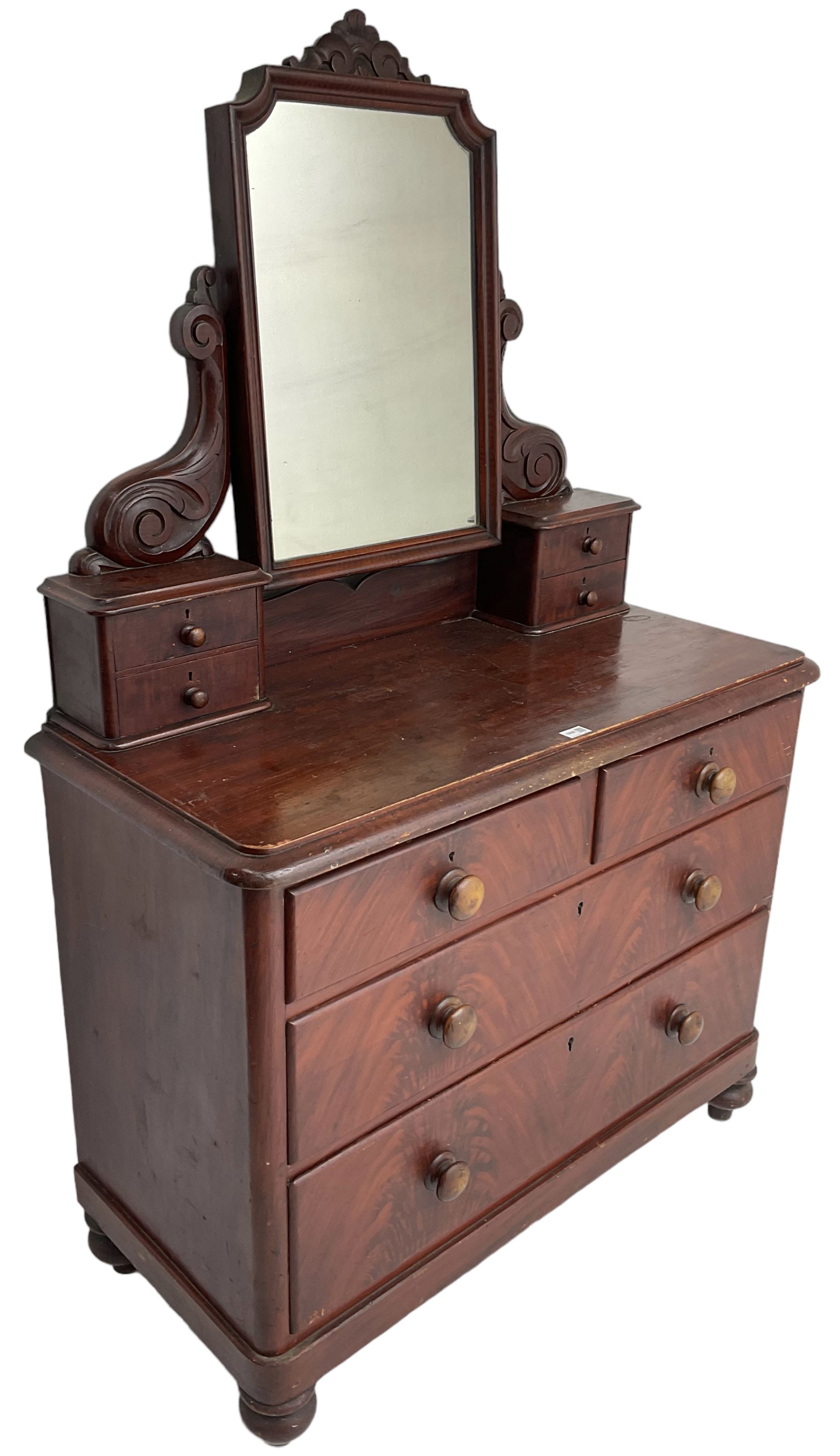 Victorian scumbled pine dressing chest, raised swing mirror in moulded frame with scrolled carved pediment, foliage S-scroll carved supports over trinket drawers, moulded rectangular top with rounded corners over two short and two long drawers, skirted base on turned feet, scumbled to resemble mahogany 