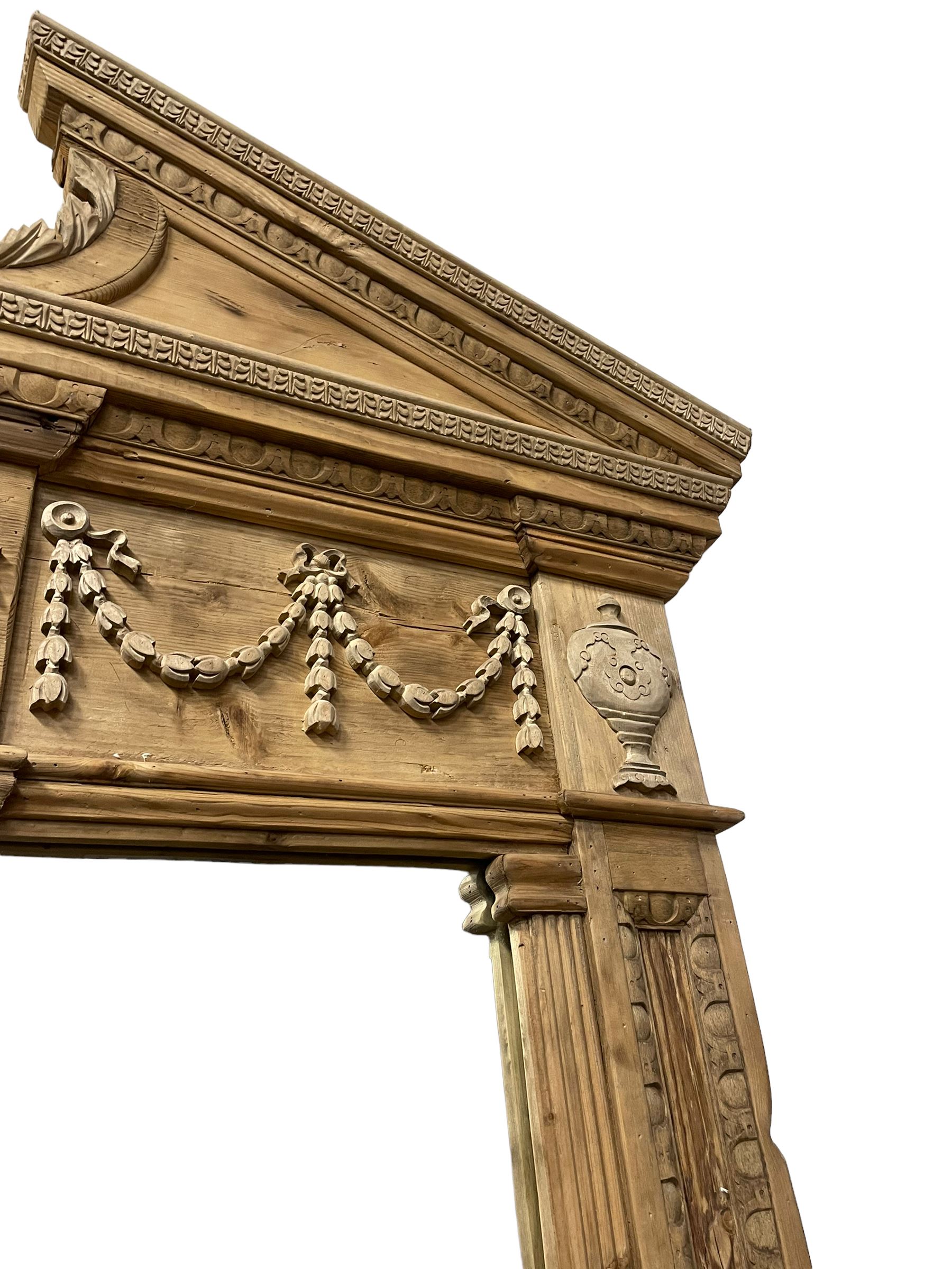 Large Adams design pine frame mirror, sloped broken arch pediment with central acanthus leaf carving, the frieze decorated with bell flower garlands and central kylix vase motif, large plain mirror plate flanked by panelled sides with egg and dart mouldings and reeded slip mouldings, on plinth base