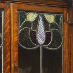 Arts and Crafts oak dresser, projecting moulded cornice above three glazed panels with coloured leaded glass floral panels, flanked by two glazed doors enclosing two adjustable shelves, open mirrored recess below with mirrored back, the base fitted with two short drawers over two central drawers flanked by carved panelled cupboard doors, ornate brass handles, raised on tapering square legs