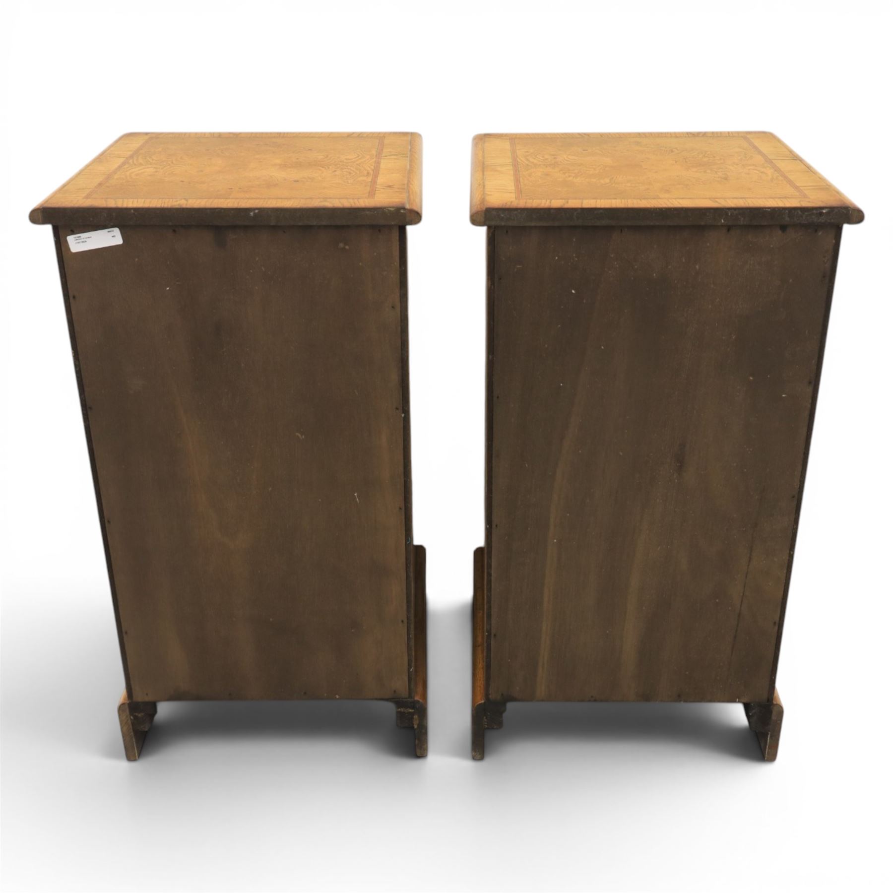 Pair of burr oak bedside tables with campaign brass handles, inlaid and crossbanded top, above four graduating drawers with cockbeaded edges, raised on a plinth base 