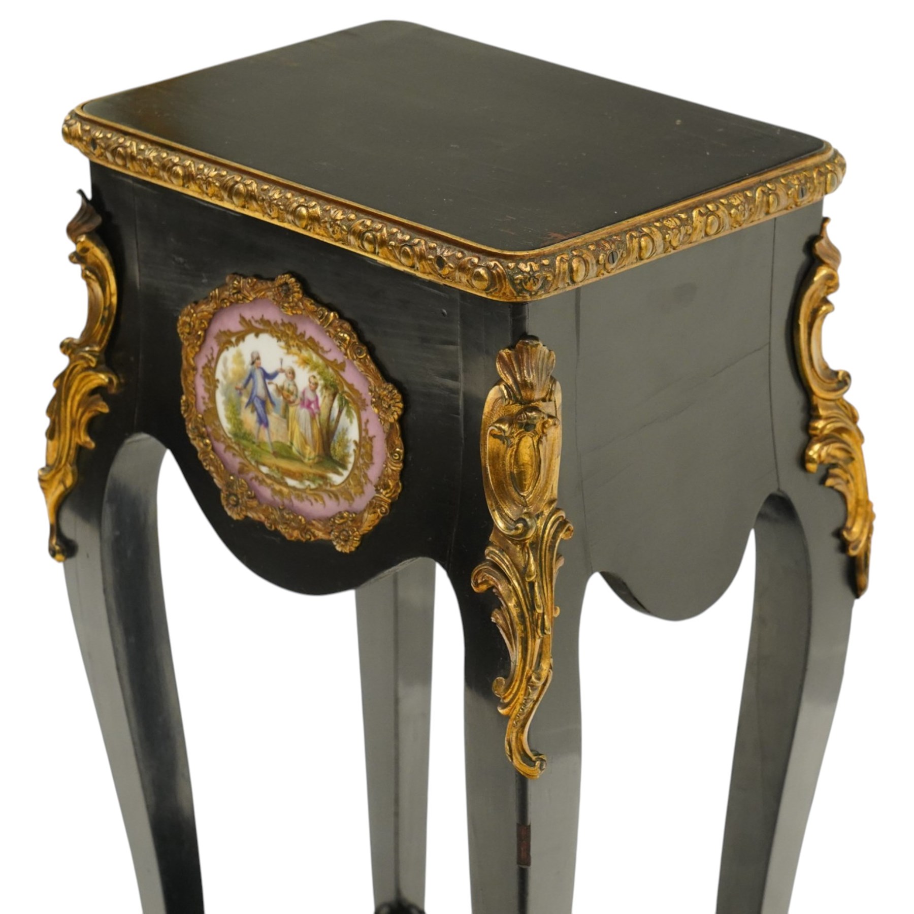 Early 20th century French ebonised sewing or work table, rectangular hinged top with foliate moulded gilt metal edge, enclosing upholstered interior, over a central Sevres style porcelain plaque depicting a courting scene, raised on cabriole supports with gilt metal carotuche and acanthus knee mounts, united by undertier with brass gallery terminating to gilt metal scroll feet
