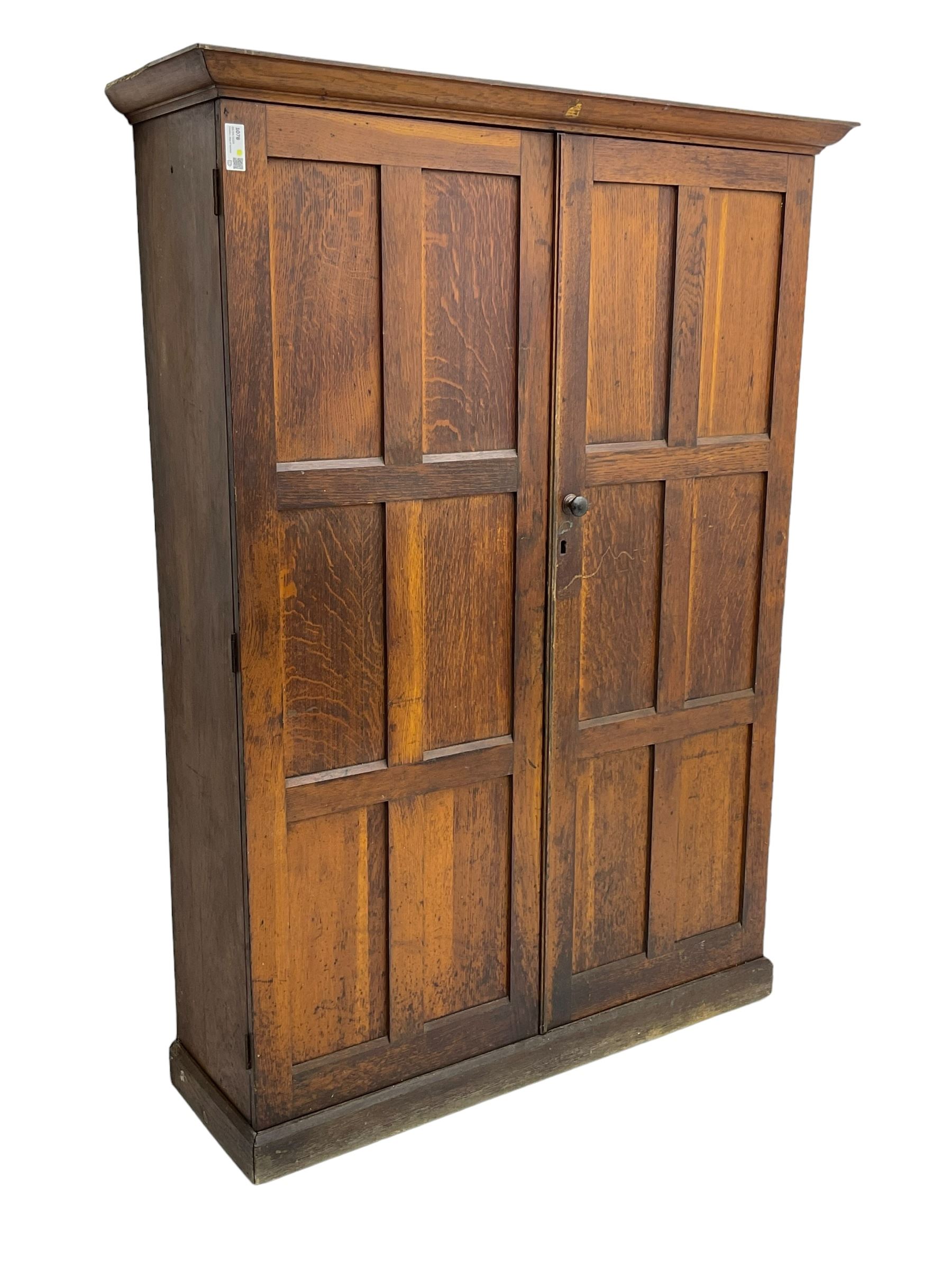 The North of England School Furnishing Company Limited Darlington - early 20th century oak school cupboard, projecting moulded cornice over two panelled doors, fitted with shelves, on chamfered plinth base 