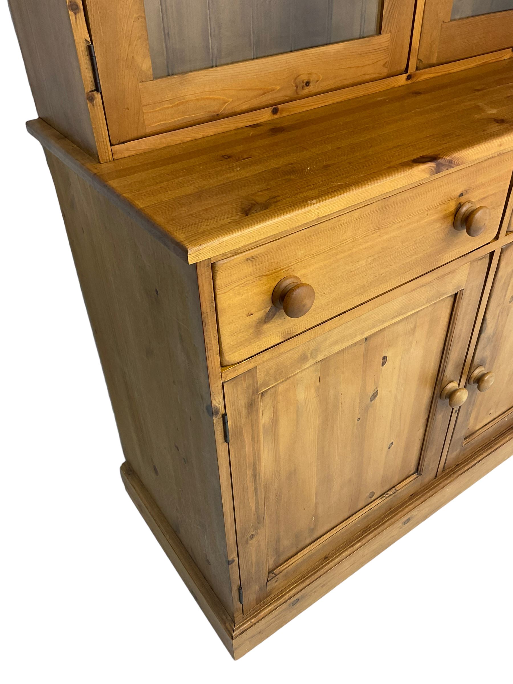 Large pine bookcase on cupboard, the upper section enclosed by two glazed door, the lower section fitted with two drawers and double cupboard, on plinth base