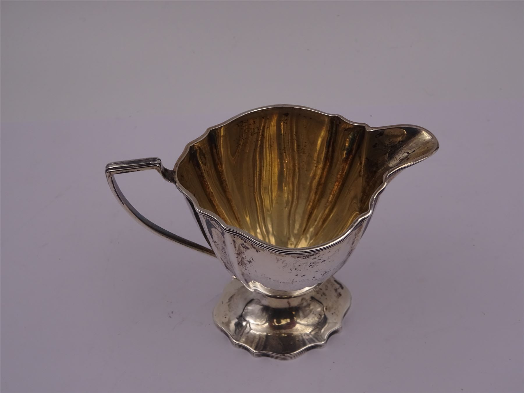 Edwardian silver cream jug, of fluted helmet form, with angular handle and upon shaped foot, hallmarked Birmingham 1905, maker's mark indistinct, together with a set of six Edwardian silver teaspoons and a pair of sugar tongs, all with scrolling embossed decoration and engraved monogram, hallmarked Joseph Rodgers & Sons, Sheffield 1903, within tooled leather fitted case, jug including handle H9cm 