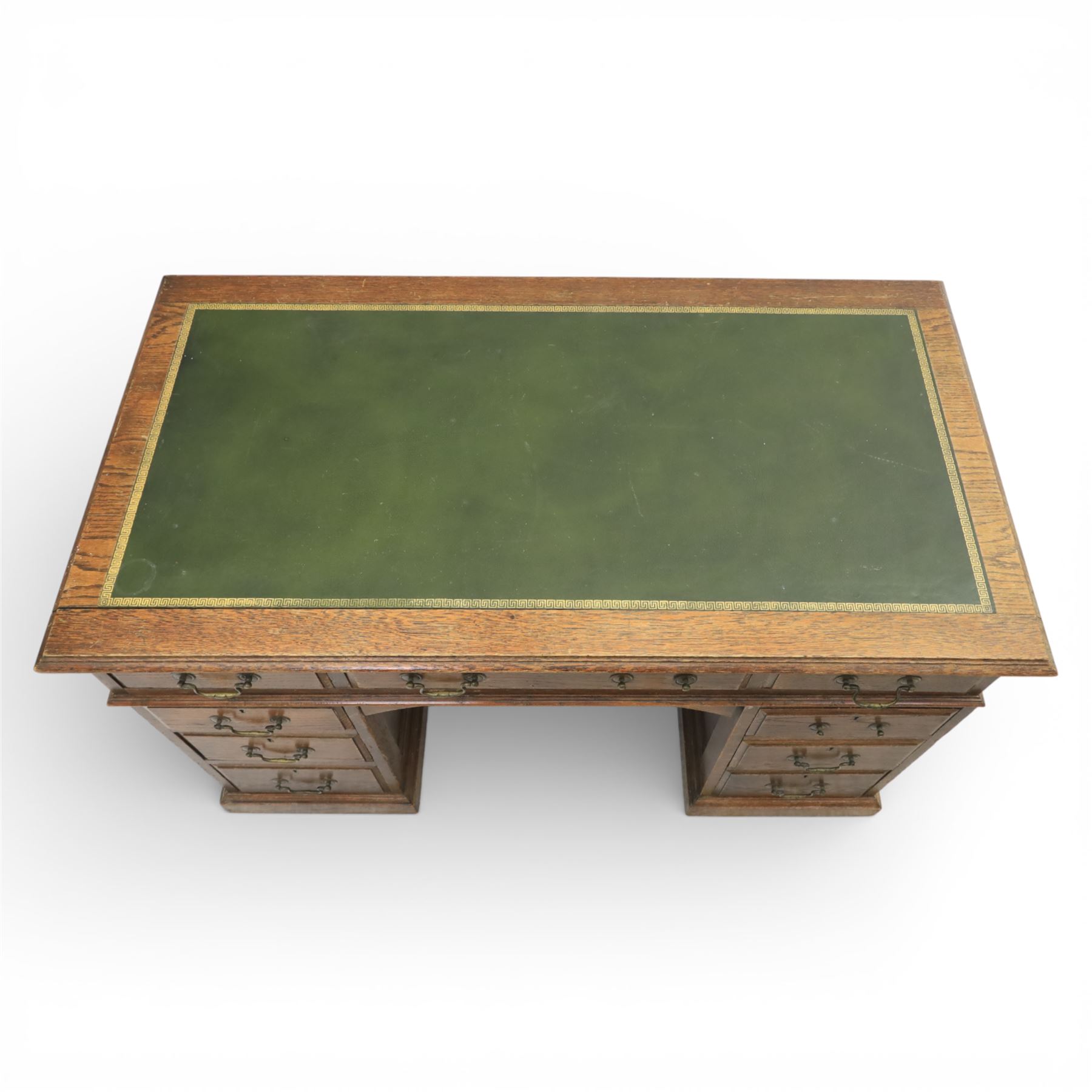 Victorian oak pedestal desk, the rectangular top with inset green leather writing panel and decorative gilt border, over a central frieze drawer flanked by two short drawers, twin pedestals each fitted with four drawers with brass handles, arched kneehole opening, standing on moulded plinth bases