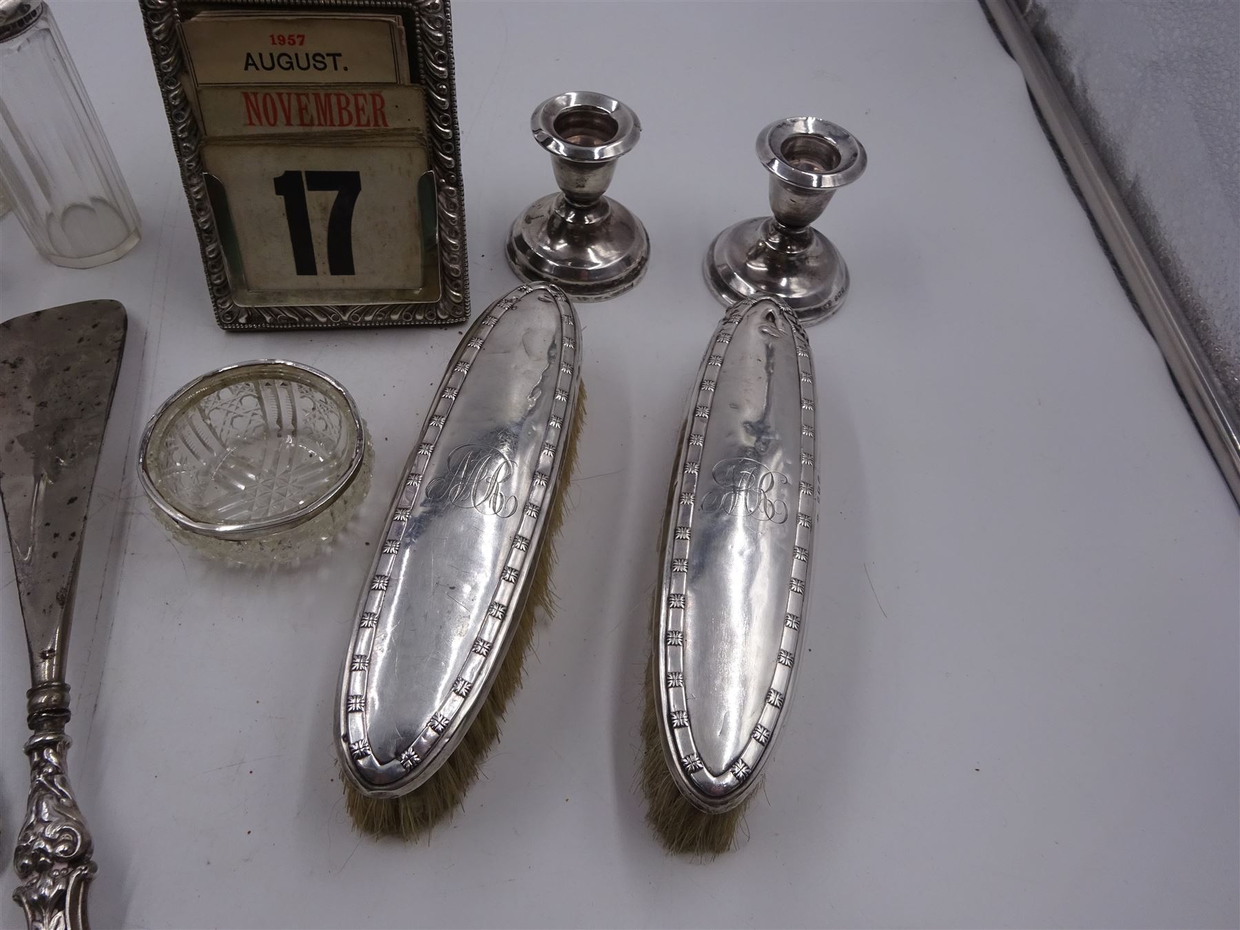 Group of silver, comprising Victorian silver mounted perpetual calendar with various date cards, hallmarked Henry Matthews, Birmingham 1900, silver mounted dressing table items, to include hair brush, with embossed decoration, pair of clothes brushes, and a shoe horn, together with a pair of silver mounted dwarf candlesticks, four cut glass jars/scent bottles with silver covers and a cut glass open salt with silver collar, all hallmarked 