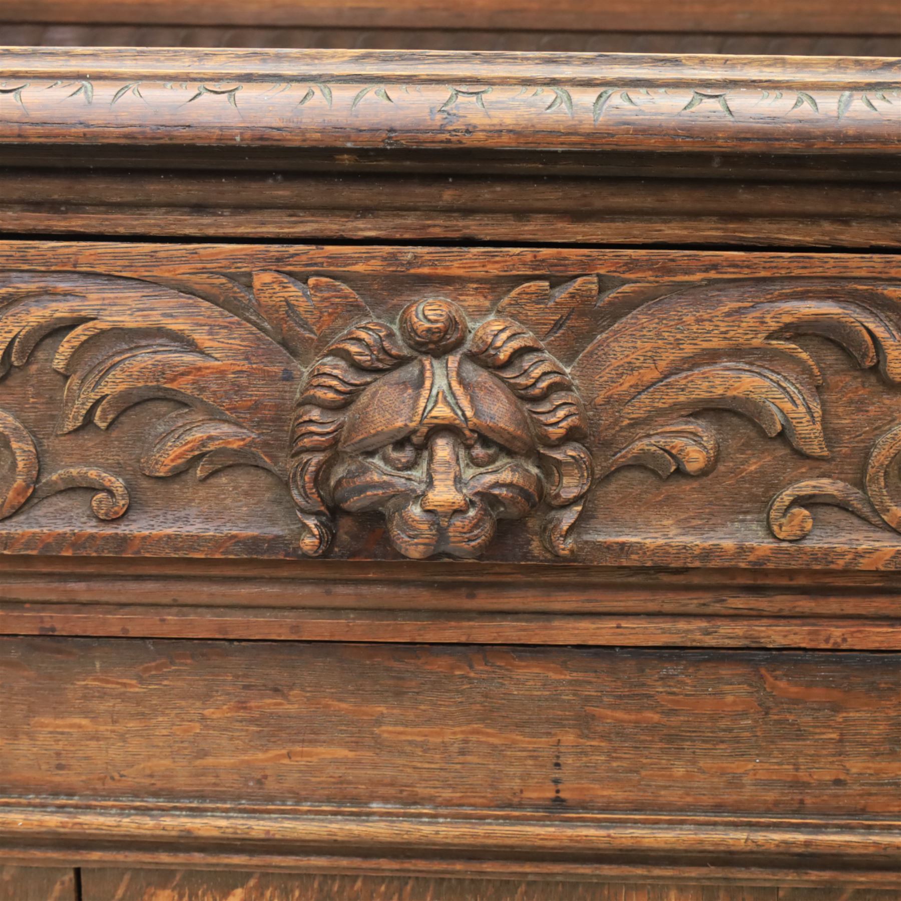 Victorian carved oak sideboard, the rectangular top with raised back carved with foliate scrolls and scroll end supports, upon a base with rectangular top with moulded edge, pair of drawers with conforming carved decoration and mask handles, and pair of carved cupboard doors, upon short stile type feet H101.5cm W183cm D54cm 