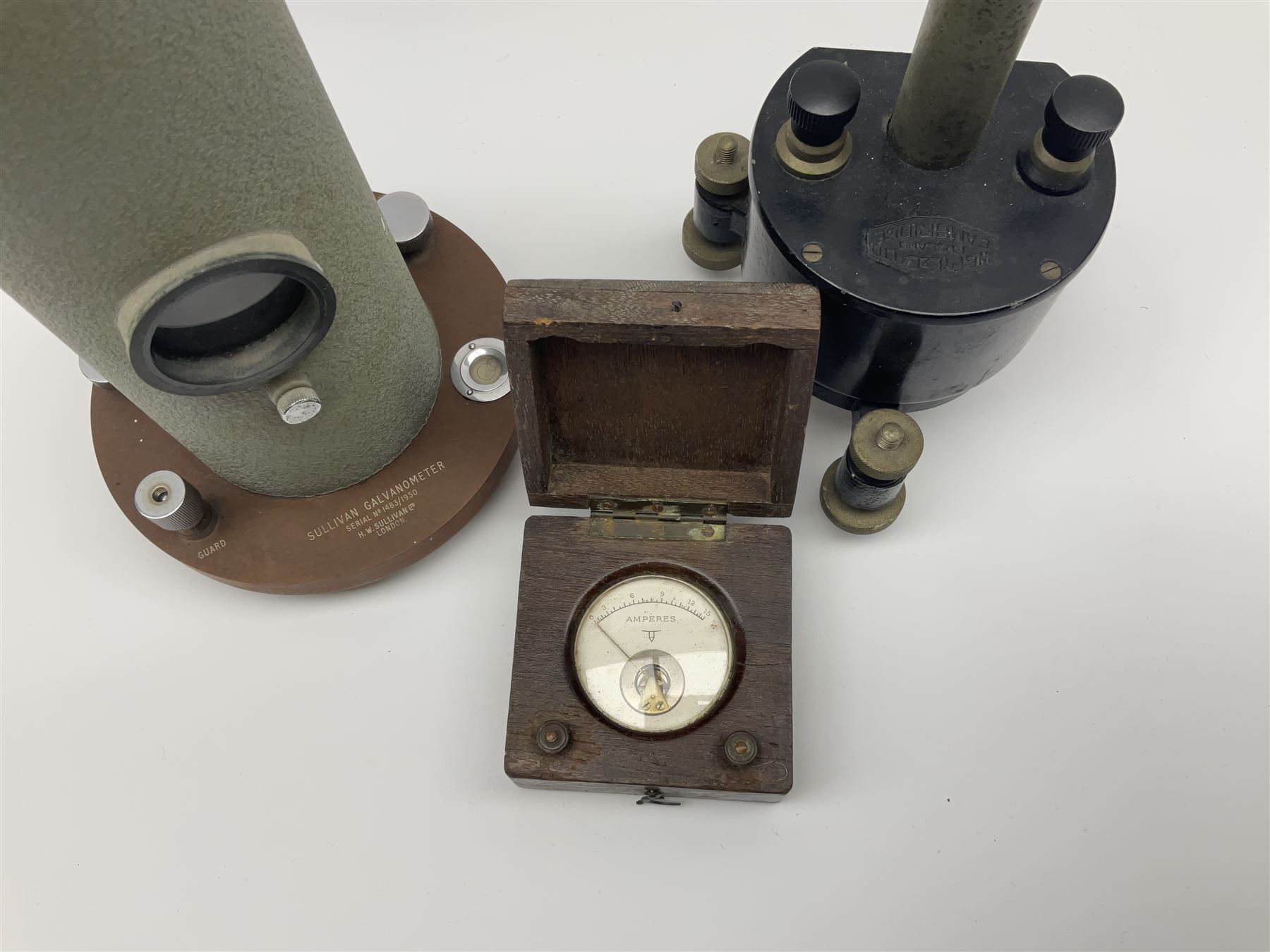 Two mirror galvanometers - one marked Sullivan Galvanometer serial no.1483/1950 of green crackled cylindrical form on circular base H24cm; the other by W.G. Pye & Co. Cambridge marked G107-131 on tripod base; together with an ammeter in wooden case (3)