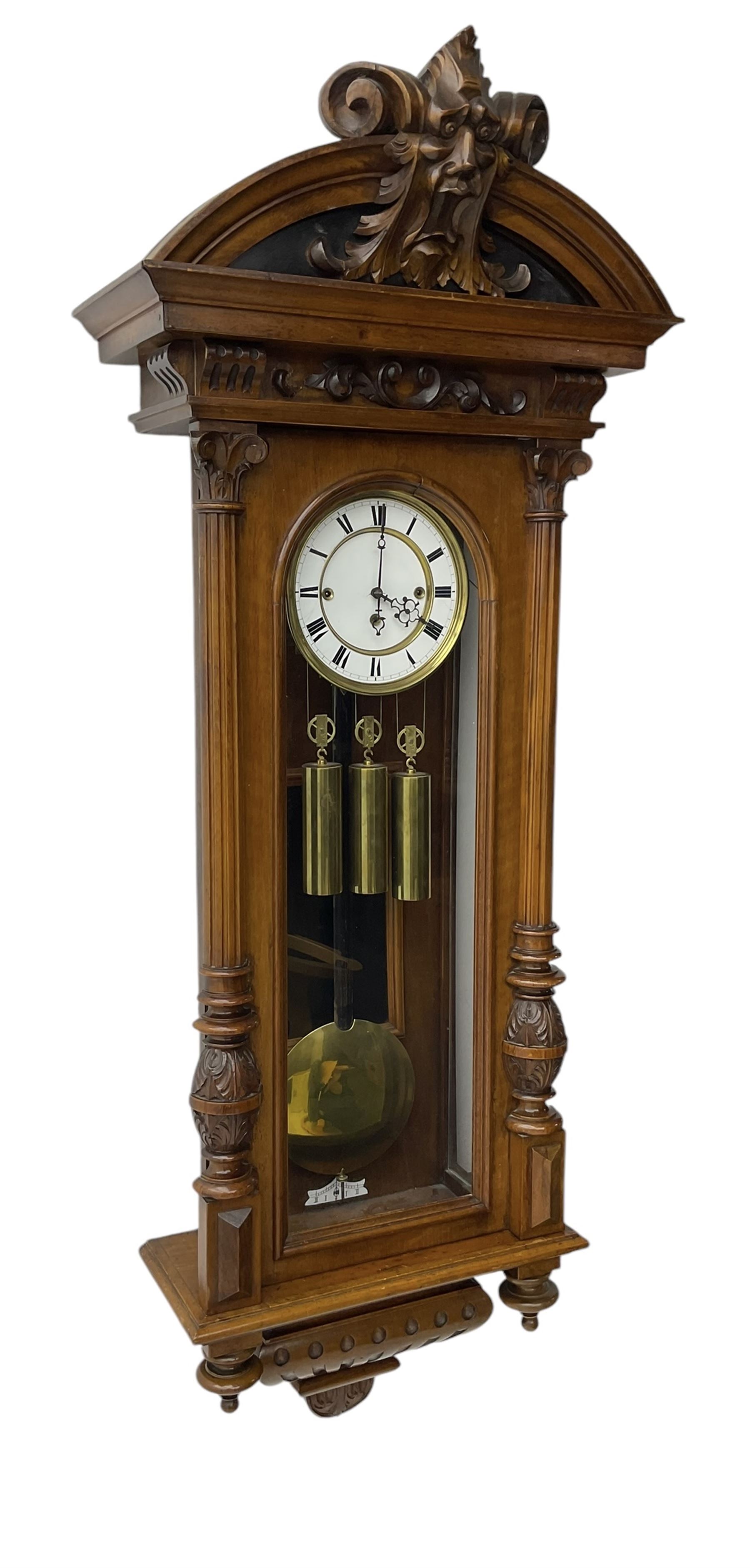 German- Late 19th century 8-day walnut cased Vienna regulator wall clock c1870,  with a broad arched pediment and heavily carved grotesque to the centre, carved frieze beneath with reeded columns to the front of the fully glazed door, carved ogee plinth and pendants to the base, two part enamel dial with Roman numerals and pierced steel hands, ebonised pendulum rod with a brass faced bob and beat plate, three matching brass cased weights and pulleys, grand sonnerie three train striking movement with a deadbeat escapement striking the quarters and hours on two coiled gongs. 
With repeat work.