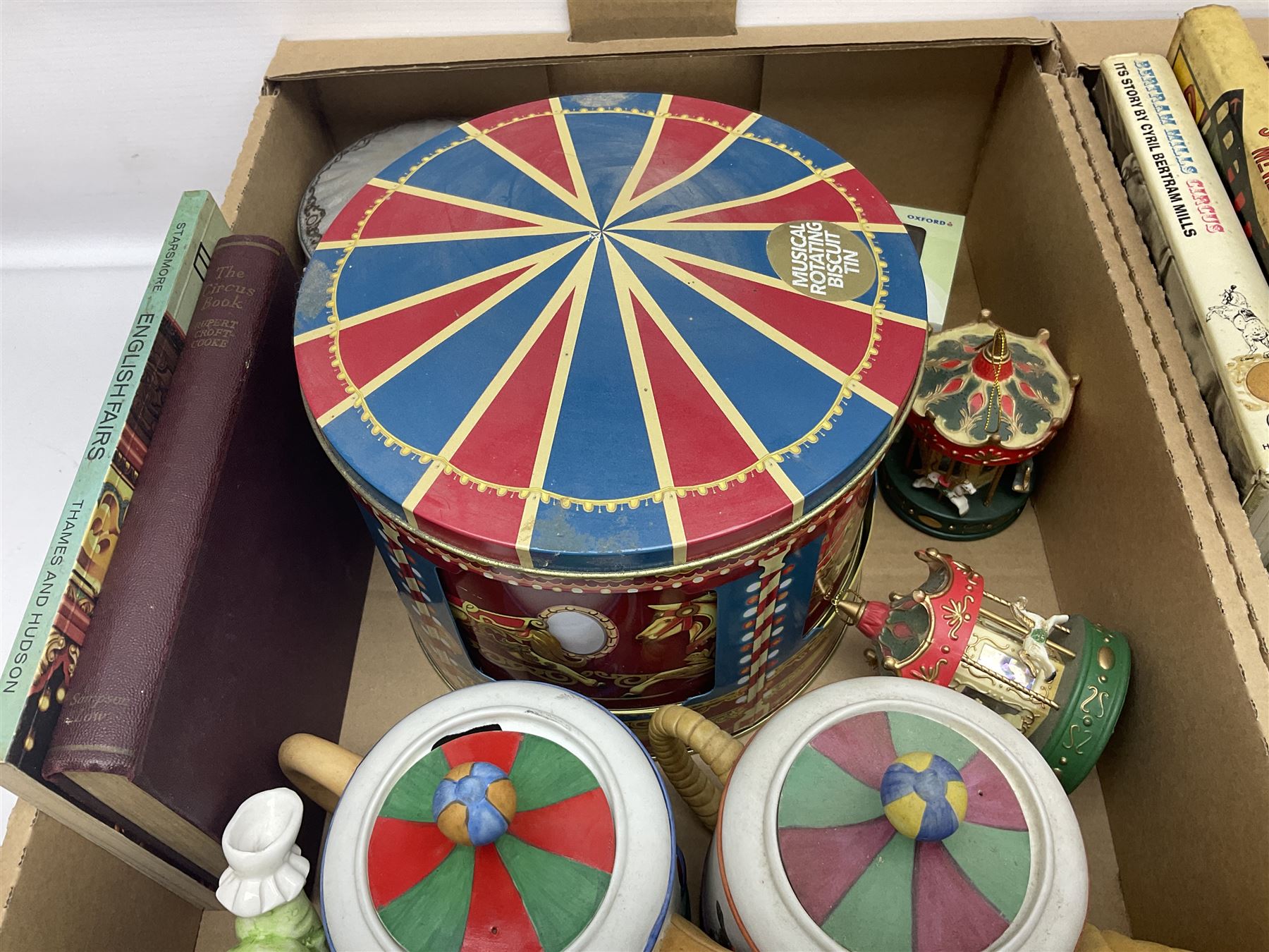 Collection of circus and fairground collectables, to include teapots, biscuit tins, including musical examples, and four Circus/fair themed books, including two library first editions