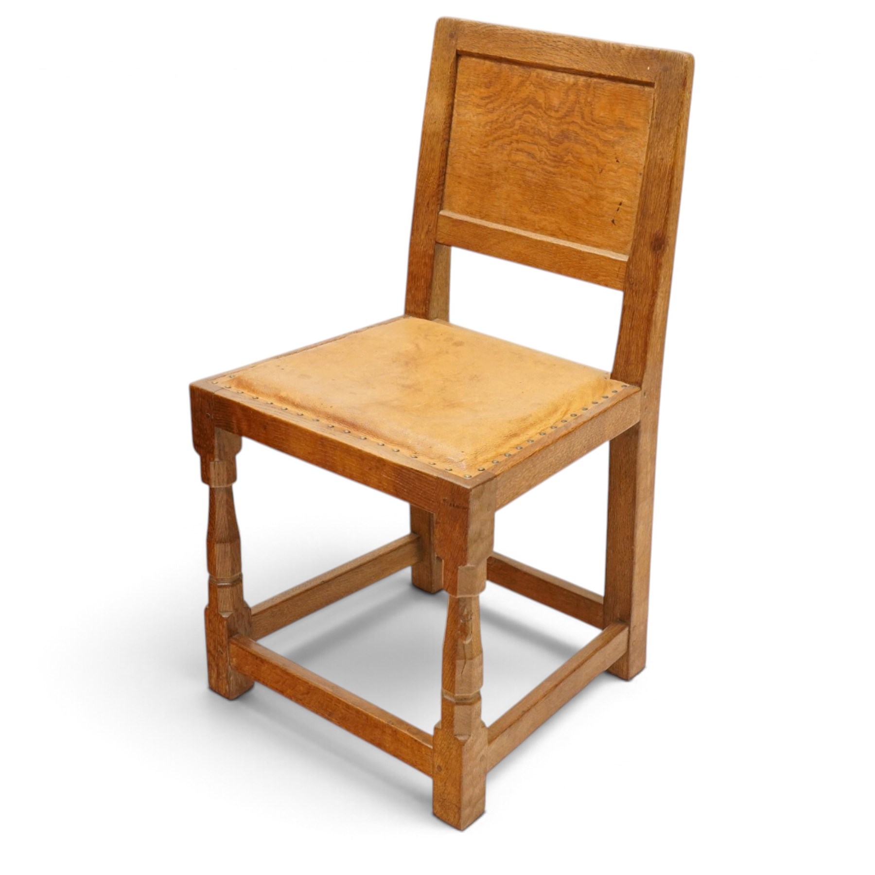 Mouseman - set of six (5+1) 1940s pre-war panel-back dining chairs, the raised backs with adzed panels, over seats upholstered in tan leather with studwork border, raised on octagonal turned baluster supports united by box stretcher, with carved mouse signature, by the workshop of Robert Thompson of Kilburn

Provenance: ordered directly from the Mouseman workshop in the 1940s before the outbreak of the war, the items were subsequently delivered after the end of war. 
