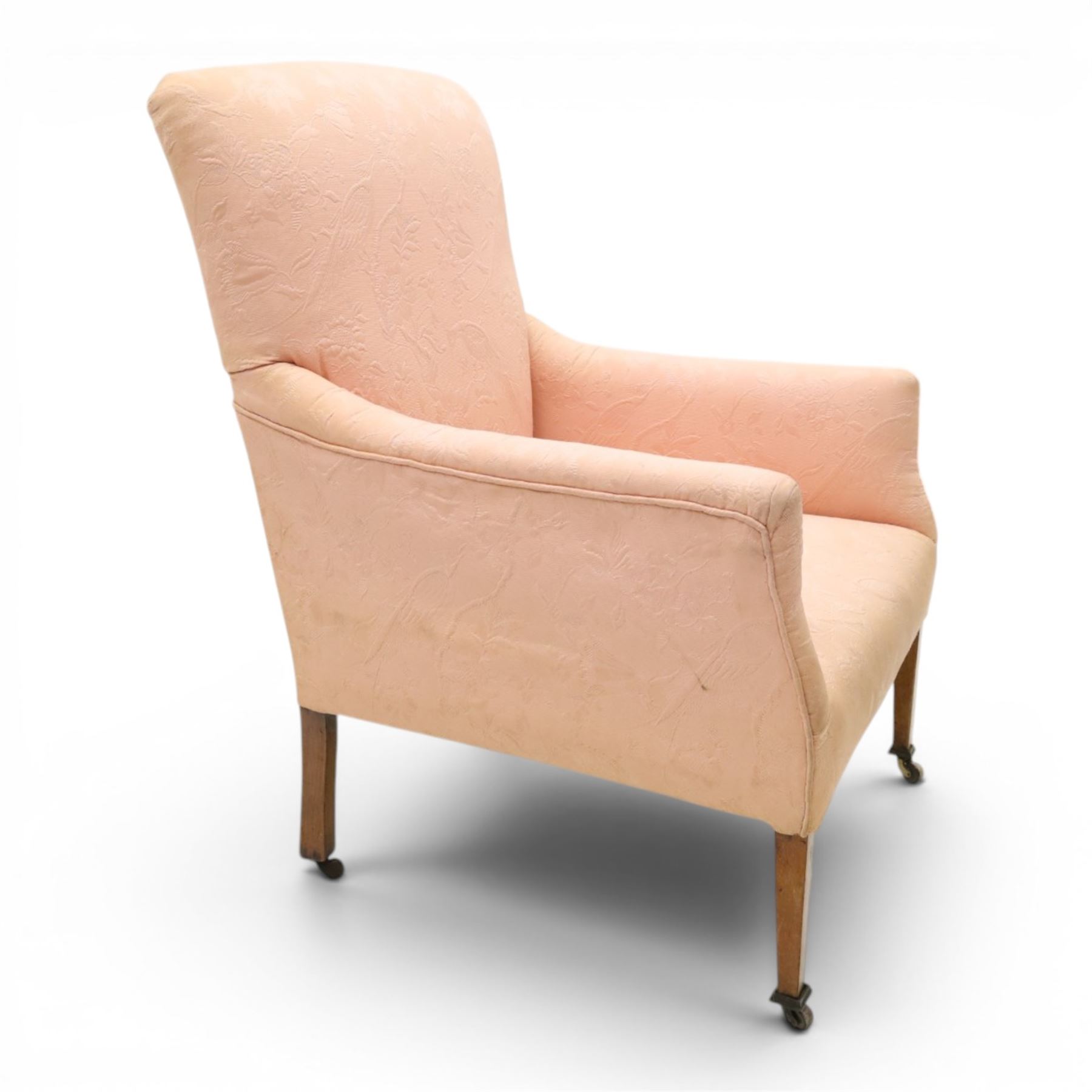 Edwardian mahogany framed armchair of traditional shape, high sprung back and seat over squared padded arms, upholstered in foliate patterned pale pink upholstery, on square tapering supports with brass castors