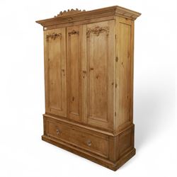 Late 19th century pine wardrobe, with stepped cornice over triple panelled doors, applied foliate carvings to outer panels, raised over a separate pine plinth drawer with moulded facia and twin glass pulls

