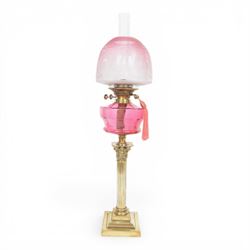 Victorian brass oil lamp, the Corinthian column supporting a cranberry glass burner and op...
