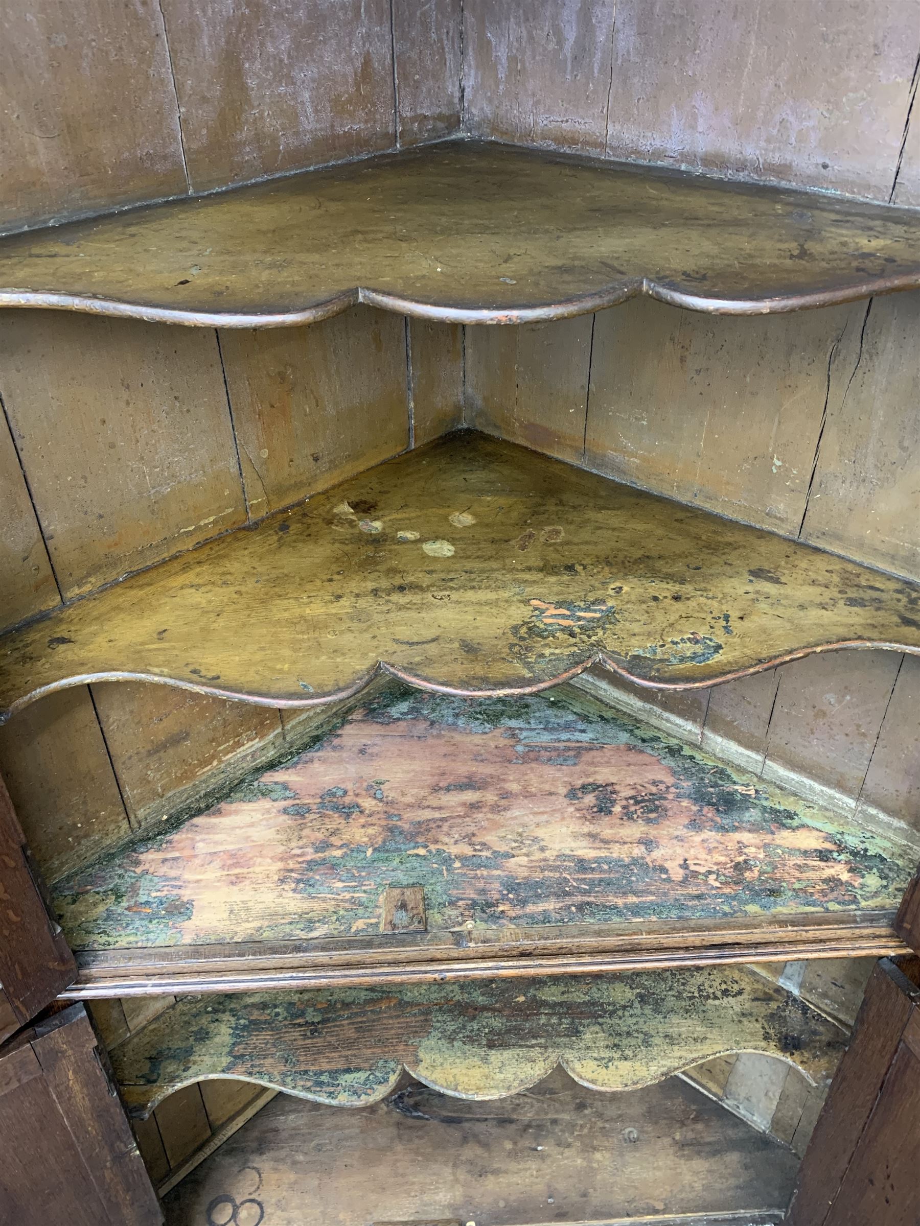 Large George III oak corner cupboard, projecting cornice over two stepped arch doors with fielded panels and blind fret work spandrels, flanked by fluted uprights, cupboard below enclosed by two fielded panel doors, the painted interior fitted with shaped shelves
 