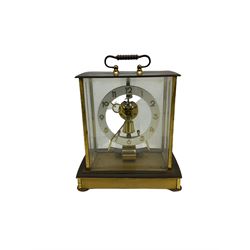 A  mid-20th century German Kieninger & Obergfell, “Kundo” battery operated 
mantle clock, rectangular case with four bevelled viewing panels and carrying handle, electrically operated solenoid pendulum powered via a battery housed in the base, skeleton movement with a visible escapement viewed through an open chapter ring with Arabic numerals and gilt baton hands.

