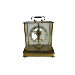 A  mid-20th century German Kieninger & Obergfell, “Kundo” battery operated 
mantle clock, rectangular case with four bevelled viewing panels and carrying handle, electrically operated solenoid pendulum powered via a battery housed in the base, skeleton movement with a visible escapement viewed through an open chapter ring with Arabic numerals and gilt baton hands.

