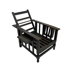 Late Victorian oak steamer chair, adjustable slatted backrest with grooved crest rail, wide armrests extending to a sliding adjustable footrest, open frame sides with vertical slats, side magazine rack and collapsible table, raised on turned front supports