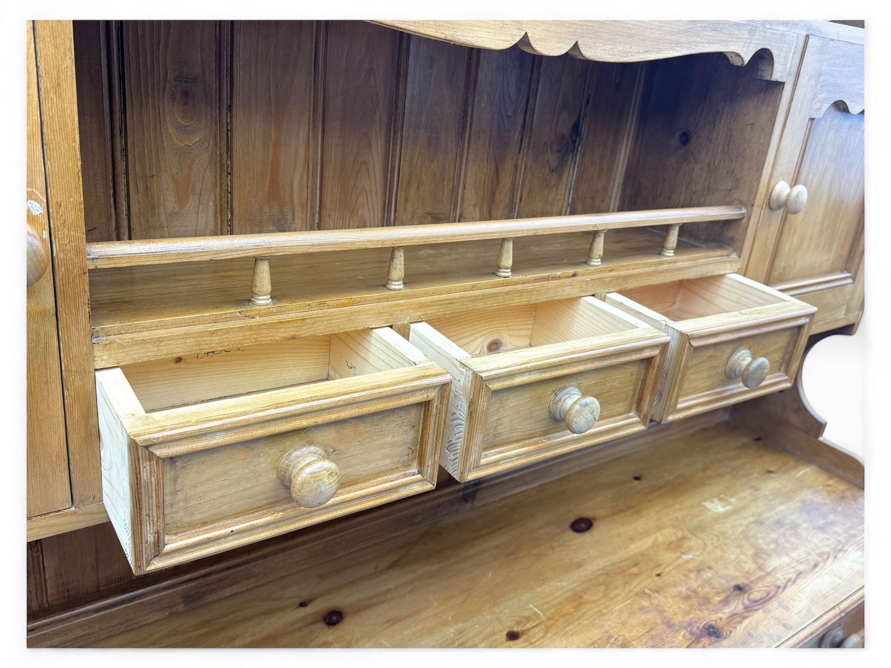 Traditional vintage pine kitchen dresser with scrolled cornice and rack with long shelf above a galleried shelf flanked by three short drawers and two cupboards, the base with three long drawers above three cupboards on plinth base  