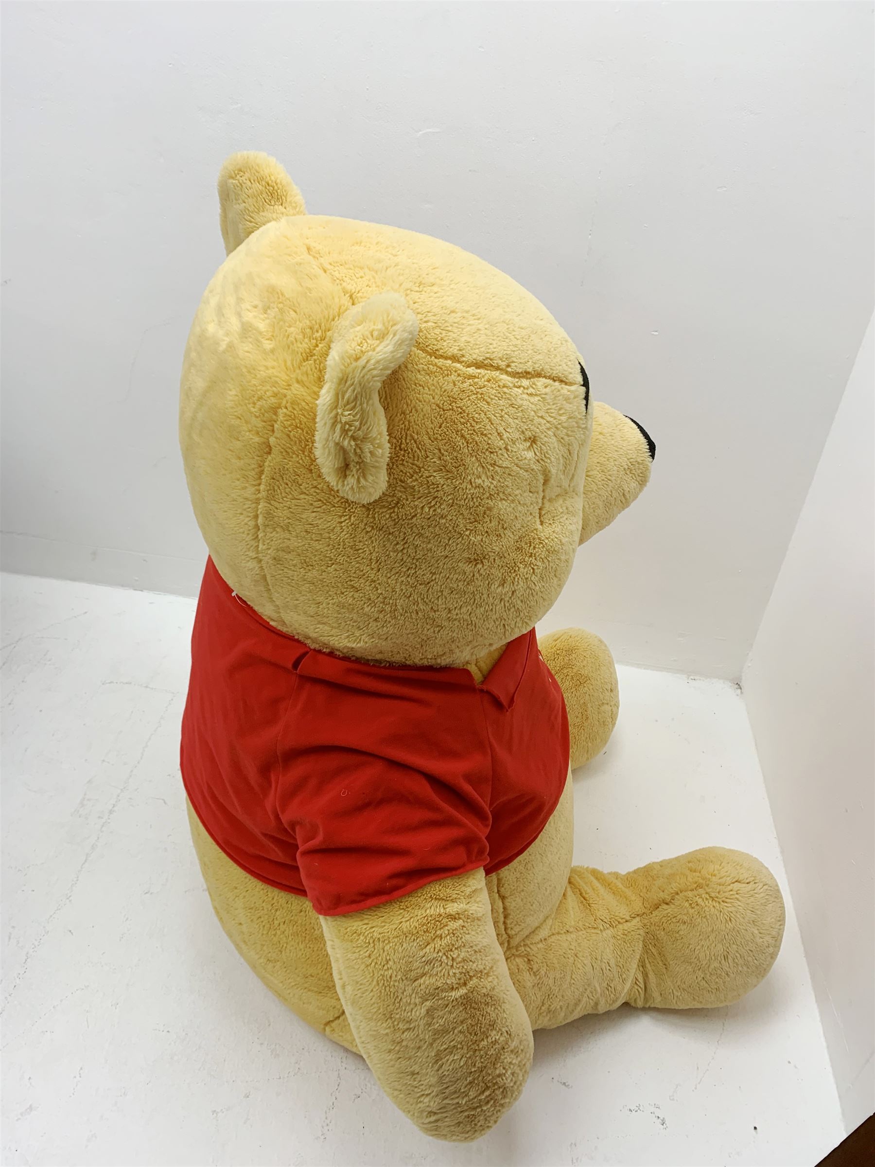 Very large plush covered figure of Winnie The Pooh in a seated position with black plastic eyes, black felt nose and eyebrows, red open mouth and T-shirt with name to front H42