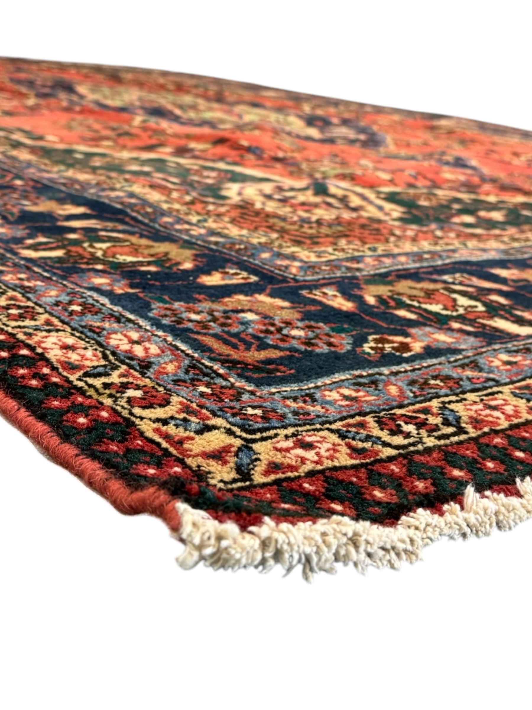 North East Persian Meshed crimson ground carpet, central indigo and green medallion with floral decoration, busy field with trailing foliage and stylised flowers, matching spandrels with floral motifs, indigo border featuring scrolling vines and palmettes, framed by narrow floral guard bands