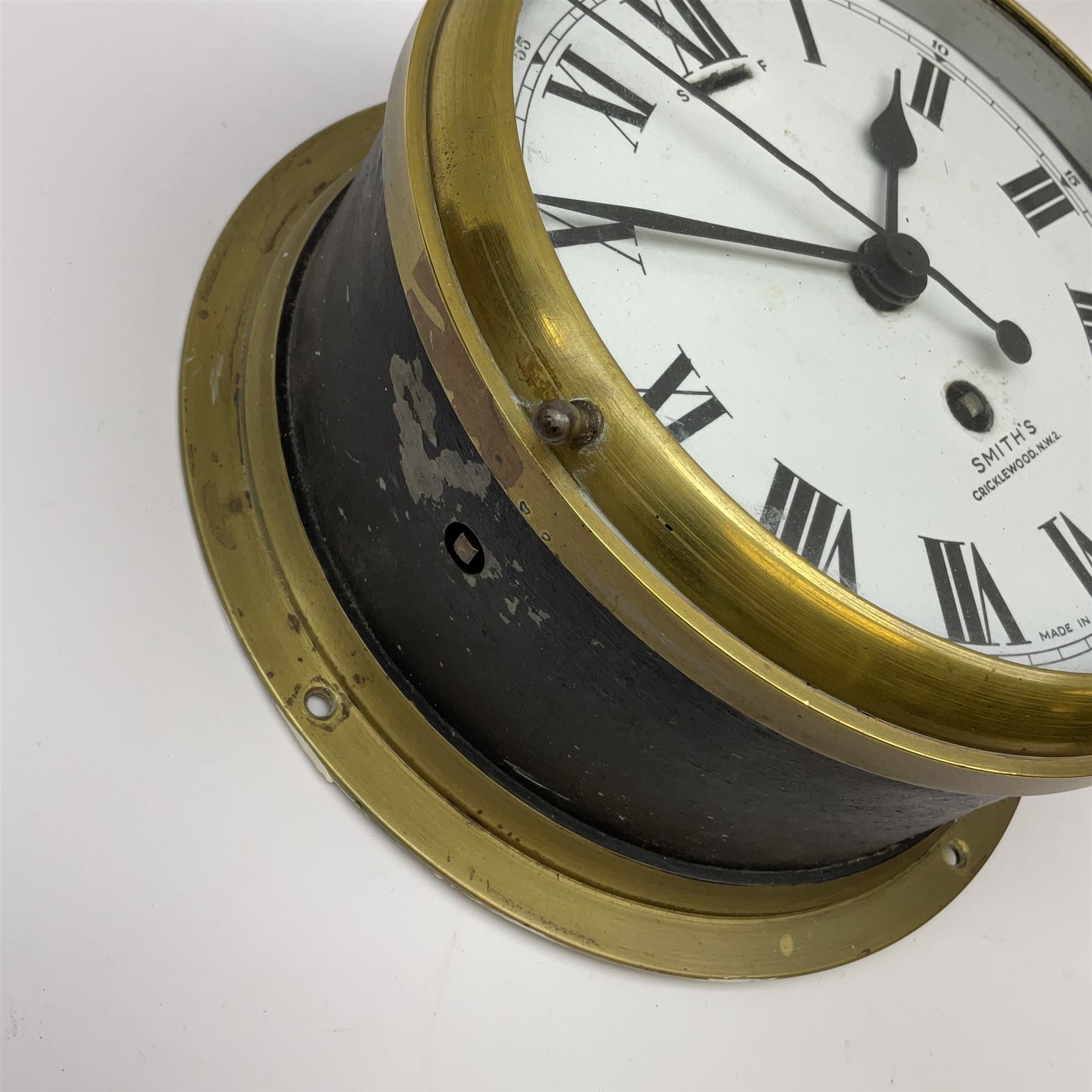 A 20th century Smiths brass cased bulkhead clock with a single train eight-day going barrel movement and balance escapement, white enamel dial with Roman numerals, minute track and five-minute Arabic’s, steel spade hands and centre second hand, dial inscribed “Smiths, Cricklewood N.W, Made in England” brass cast bezel with lock and key, flat glass with silvered sight ring, slow fast balance regulation.
Case diameter 22cm, bezel diameter 19cm.
With key
