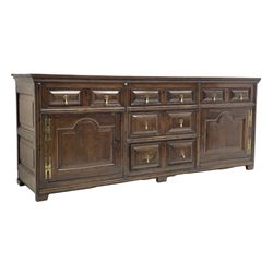 18th century oak dresser base, rectangular two plank top over drawers and cupboards, the drawer fronts mounted with geometric faceted panels with applied mouldings, the cupboards enclosed by doors with stepped arch fielded panels, on stile supports, W209cm, H85cm, D55cm