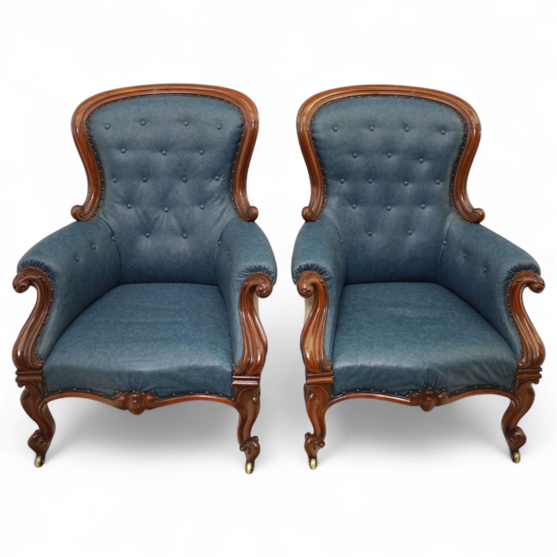 Fine pair of mid-19th-century mahogany library armchairs, carved frame with balloon-shaped back with scrolled ends, rolled wide arms, ending in a scrolled volute above a serpentine seat rail, upholstered in mottled turquoise faux leather, button upholstered back, arms, and cushion seat, studded sides and apron, raised on scroll carved front feet and splayed rear legs on castors 