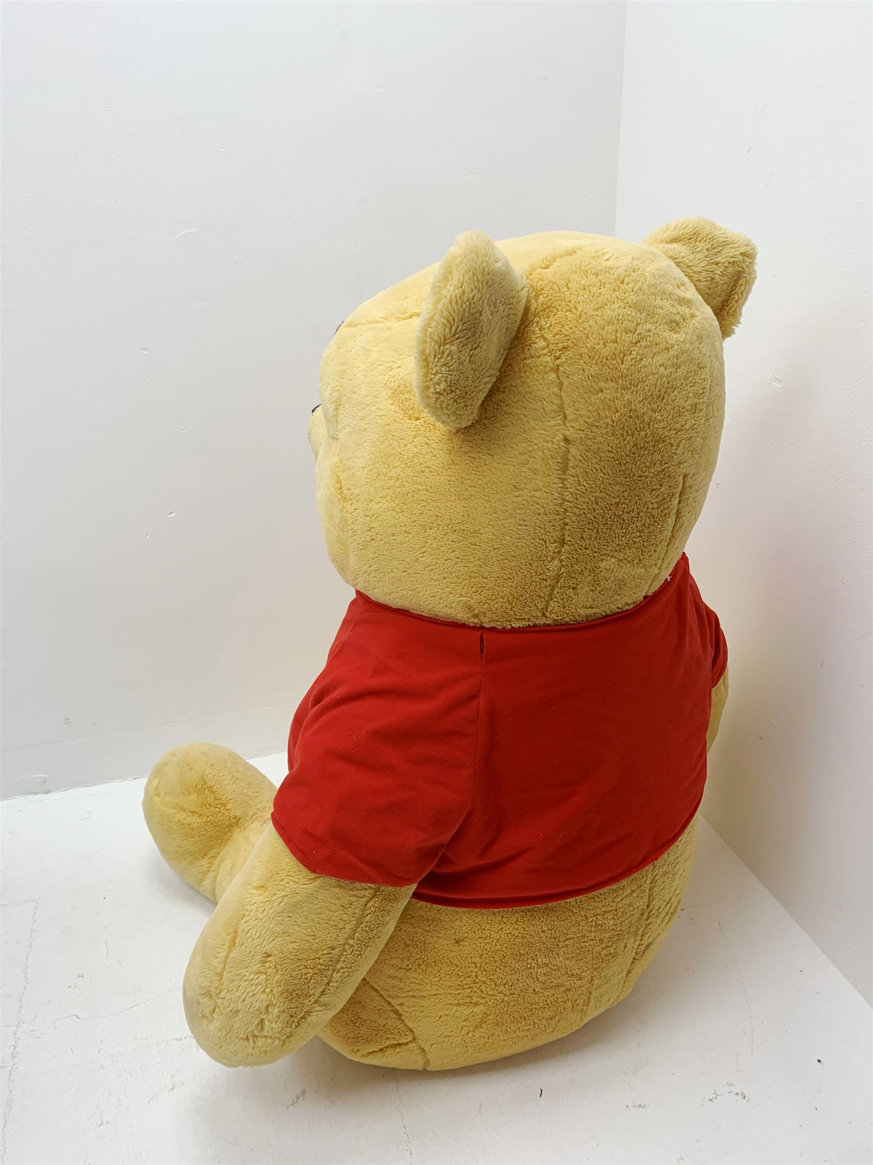 Very large plush covered figure of Winnie The Pooh in a seated position with black plastic eyes, black felt nose and eyebrows, red open mouth and T-shirt with name to front H42