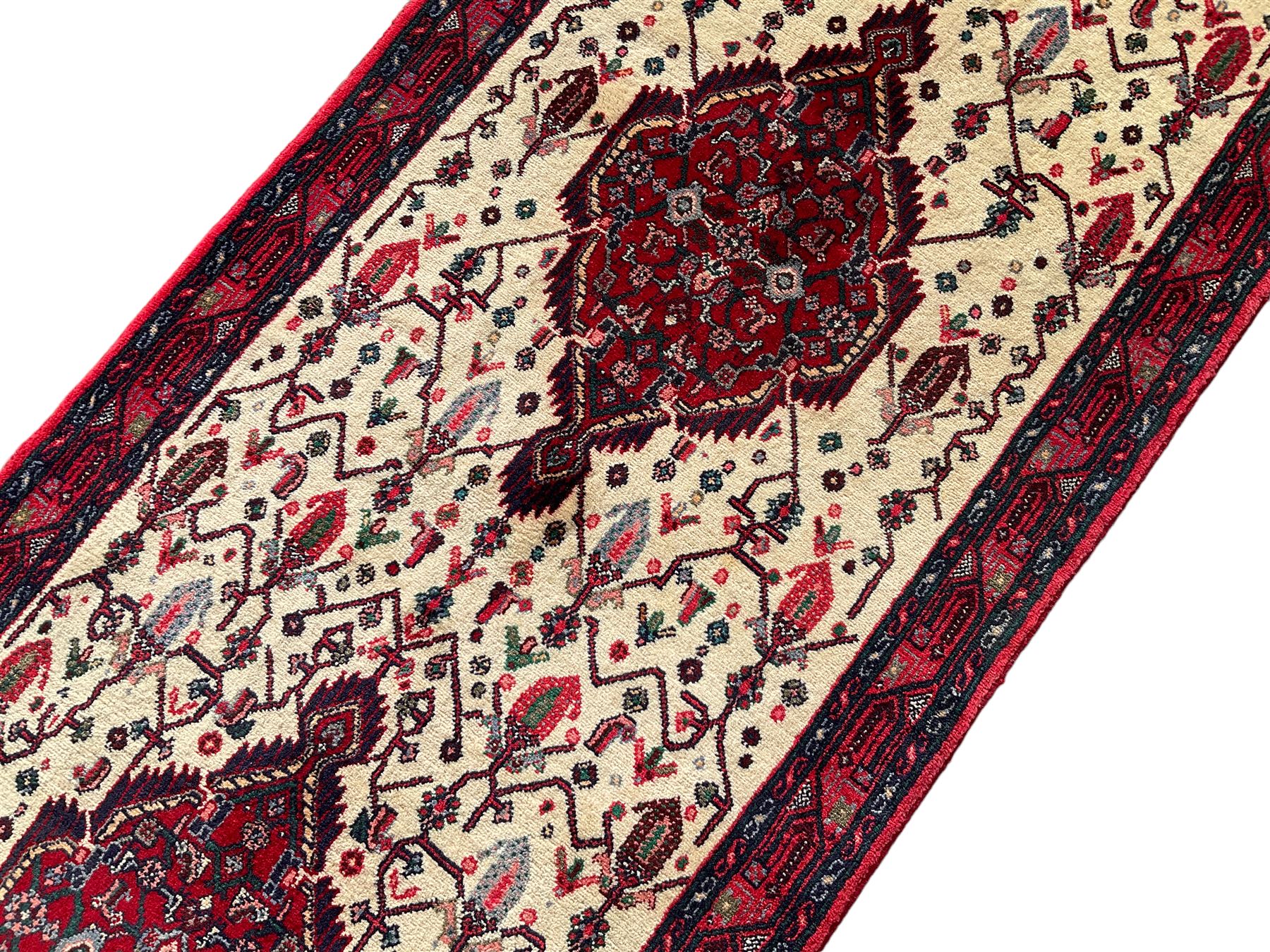 North West Persian Saveh crimson ground runner rug, the three lozenge pole medallions in an ivory field, surrounded by stylised plant motifs, the guarded border decorated with repeating geometric patterns
