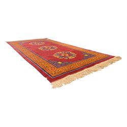 Tibetan-design handwoven rug, deep red field with three central medallions in yellow and blue, traditional yellow key border, white fringes on both ends