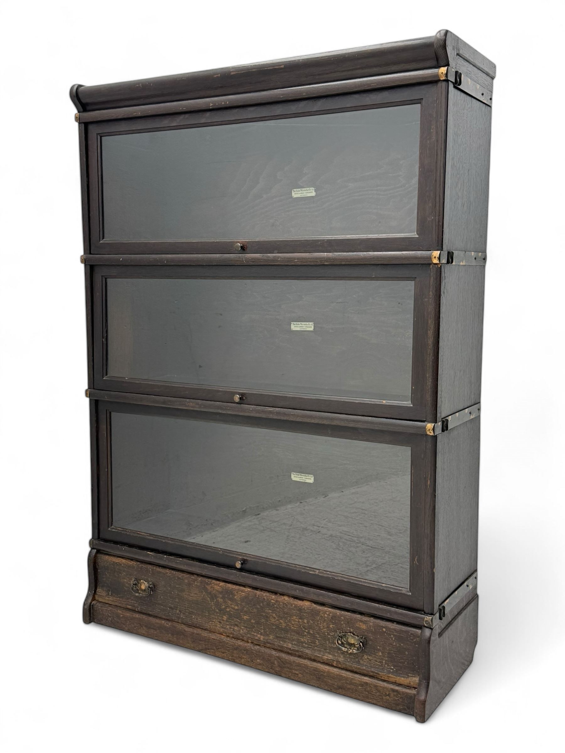 Globe Wernicke - early 20th century oak three-tier stacking library bookcase, three glazed sections enclosed by hinged and sliding doors, raised above a single lower drawer with metal drop handles