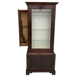 Mahogany display cabinet with hidden compartment, projecting cornice over single glazed door enclosing glass shelves, double panelled cupboard below, the interior with button releasing sliding back compartment, on bracket feet