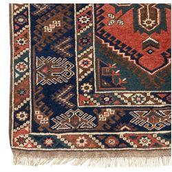 Caucasian Kazak rug, red field with three bold geometric medallions in dark blue, cream and brown, scattered tribal motifs, broad indigo border decorated with stylised hooked forms and multiple narrow patterned borders