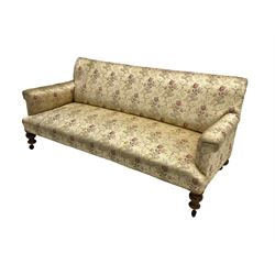 Victorian three seat sofa, upholstered in floral and scrolling foliate patterned fabric with sprung seat, raised on turned supports with castors