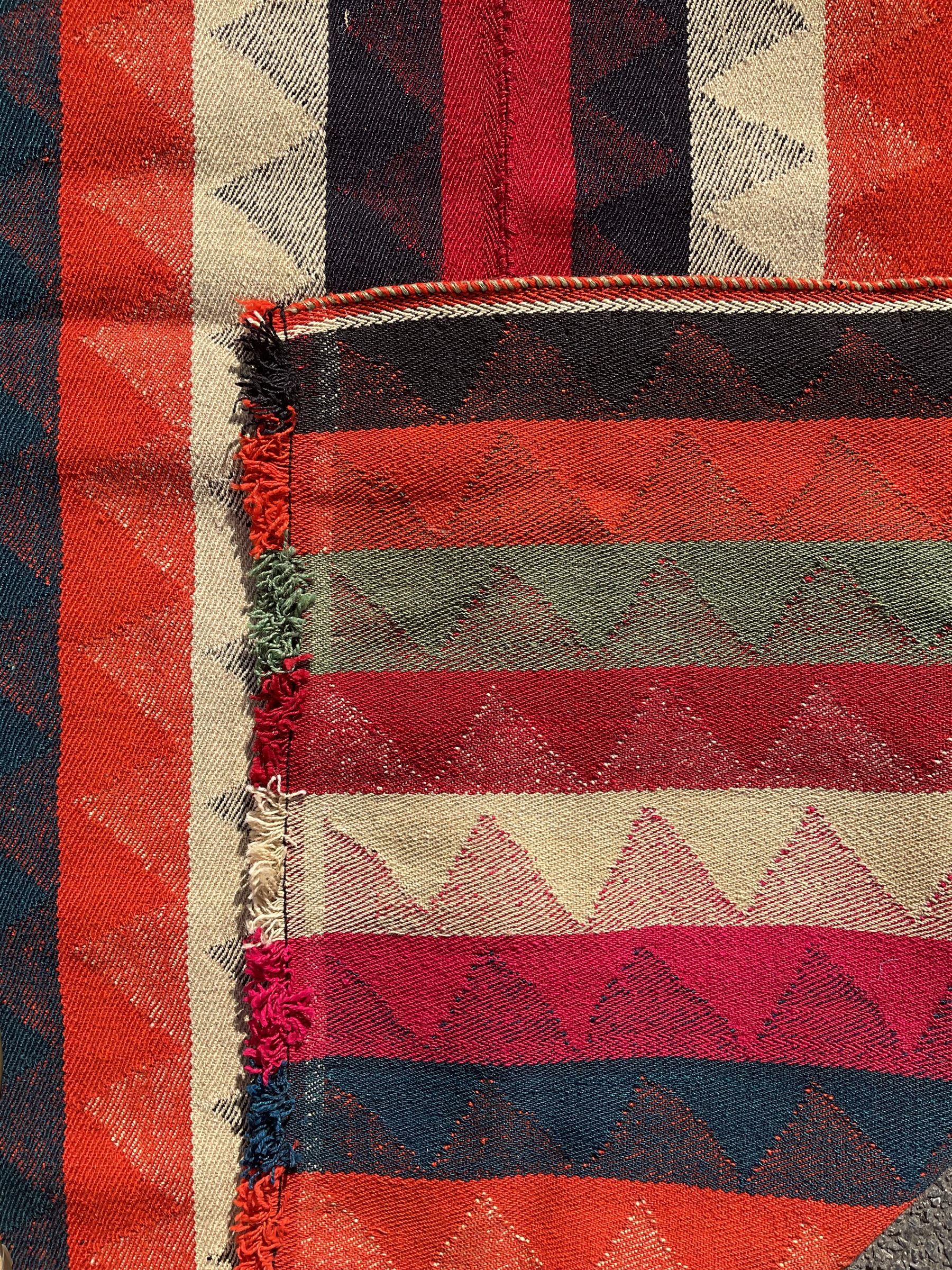 Southwest Persian Jajim Kilim ground rug, decorated with alternating vertical stripes in shades of crimson, orange, green, and black, with subtle triangular motifs woven into each stripe, bordered by narrow bands