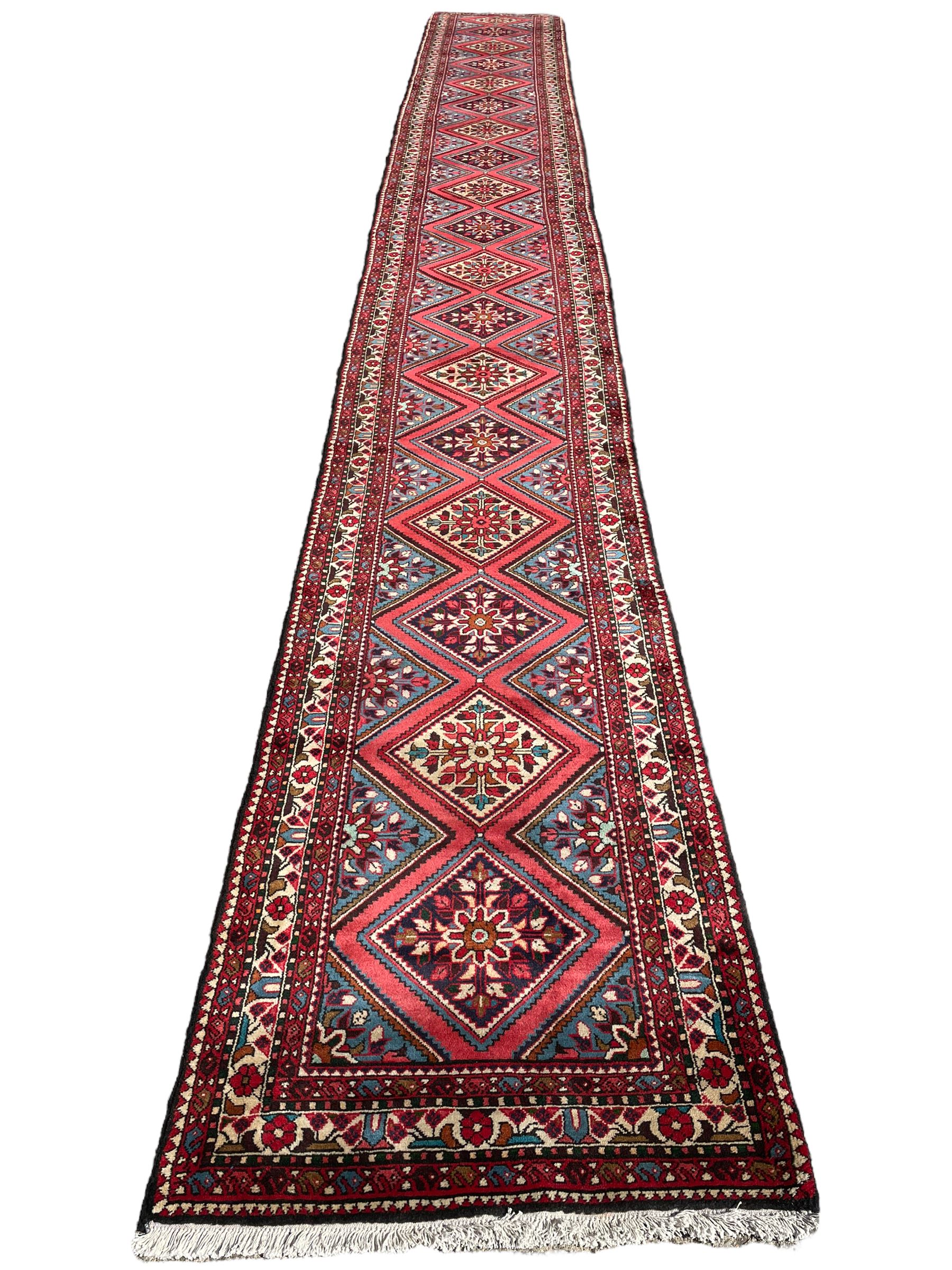 Persian Hamadan runner, red ground, decorated with eighteen lozenge medallions decorated with stylised floral motifs, three band border decorated with plant motifs and geometric patterns