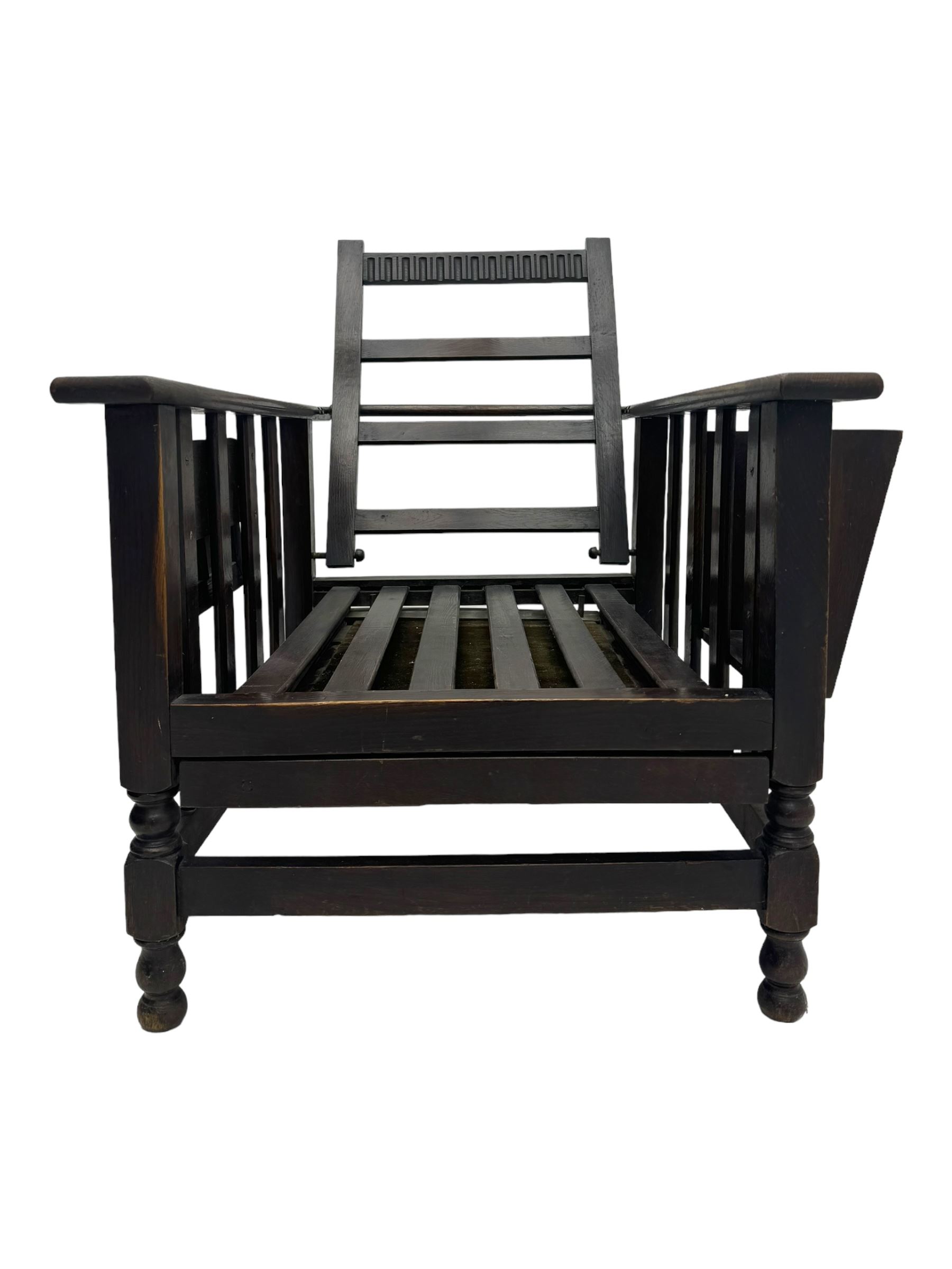 Late Victorian oak steamer chair, adjustable slatted backrest with grooved crest rail, wide armrests extending to a sliding adjustable footrest, open frame sides with vertical slats, side magazine rack and collapsible table, raised on turned front supports